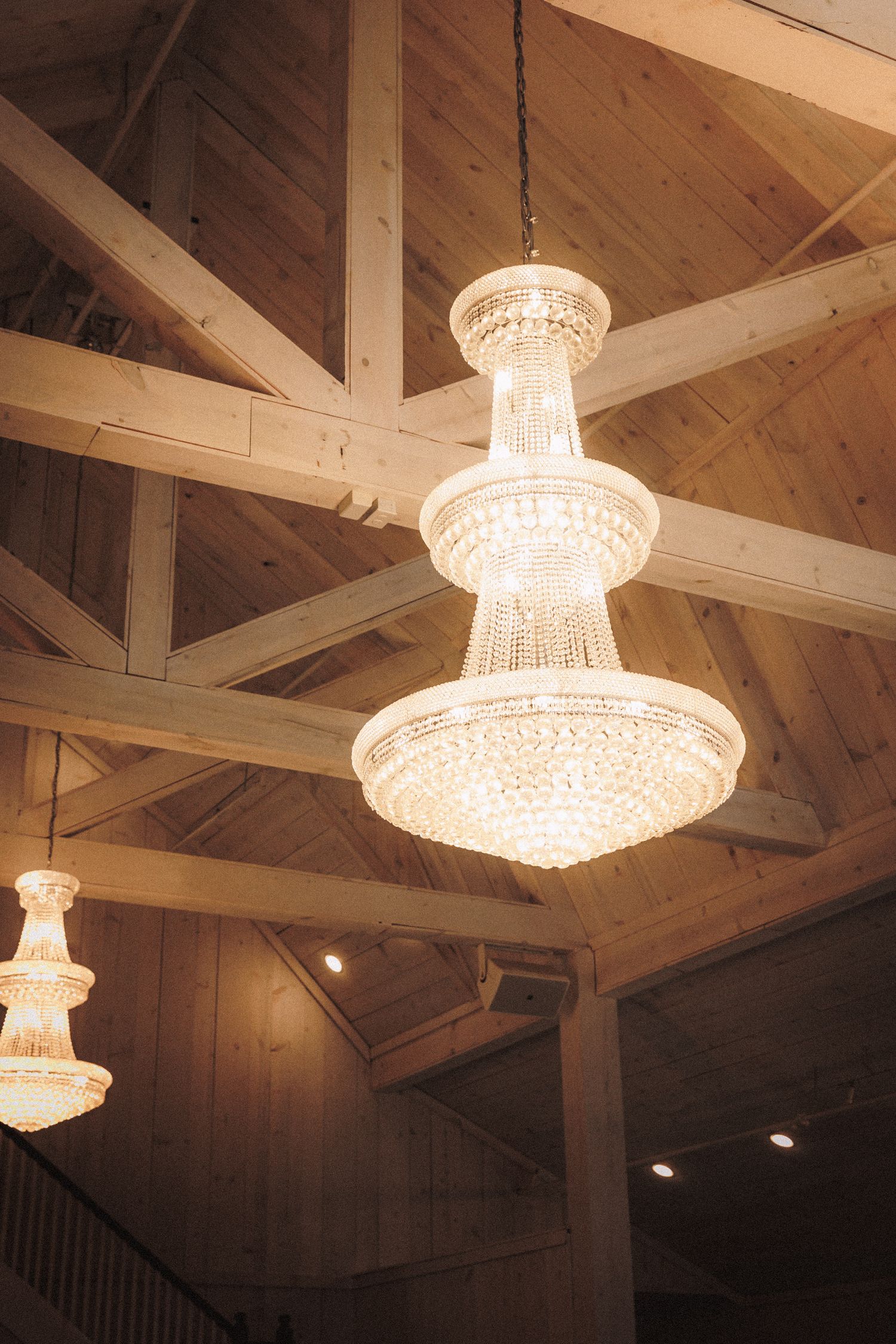 Elegant crystal chandelier hanging from rustic wooden beam ceiling in a wedding venue.