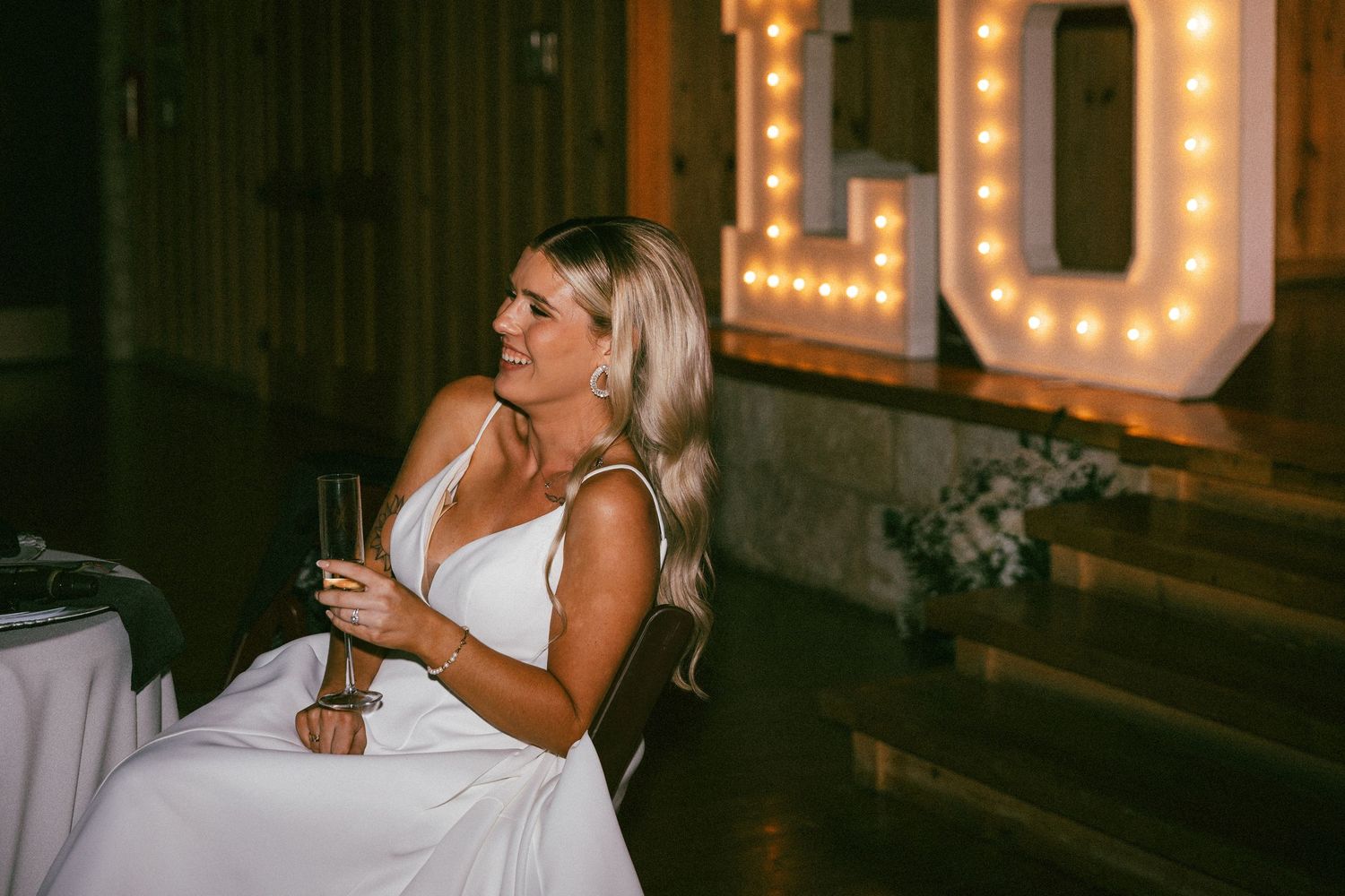 A smiling bride in a white gown holds a champagne glass at the wedding reception.