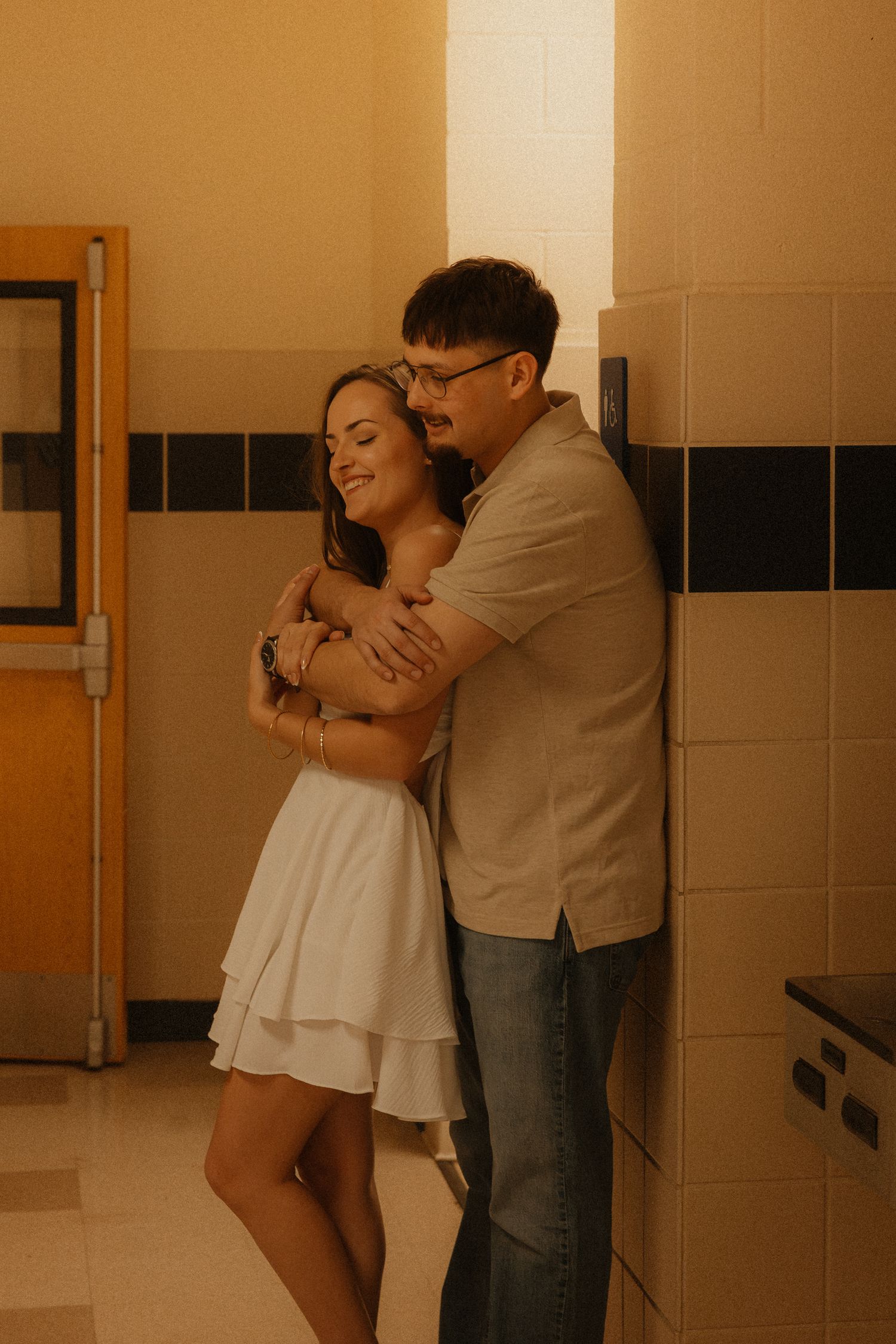 Happy couple embracing warmly in a tiled hallway, woman in white dress smiling joyfully.