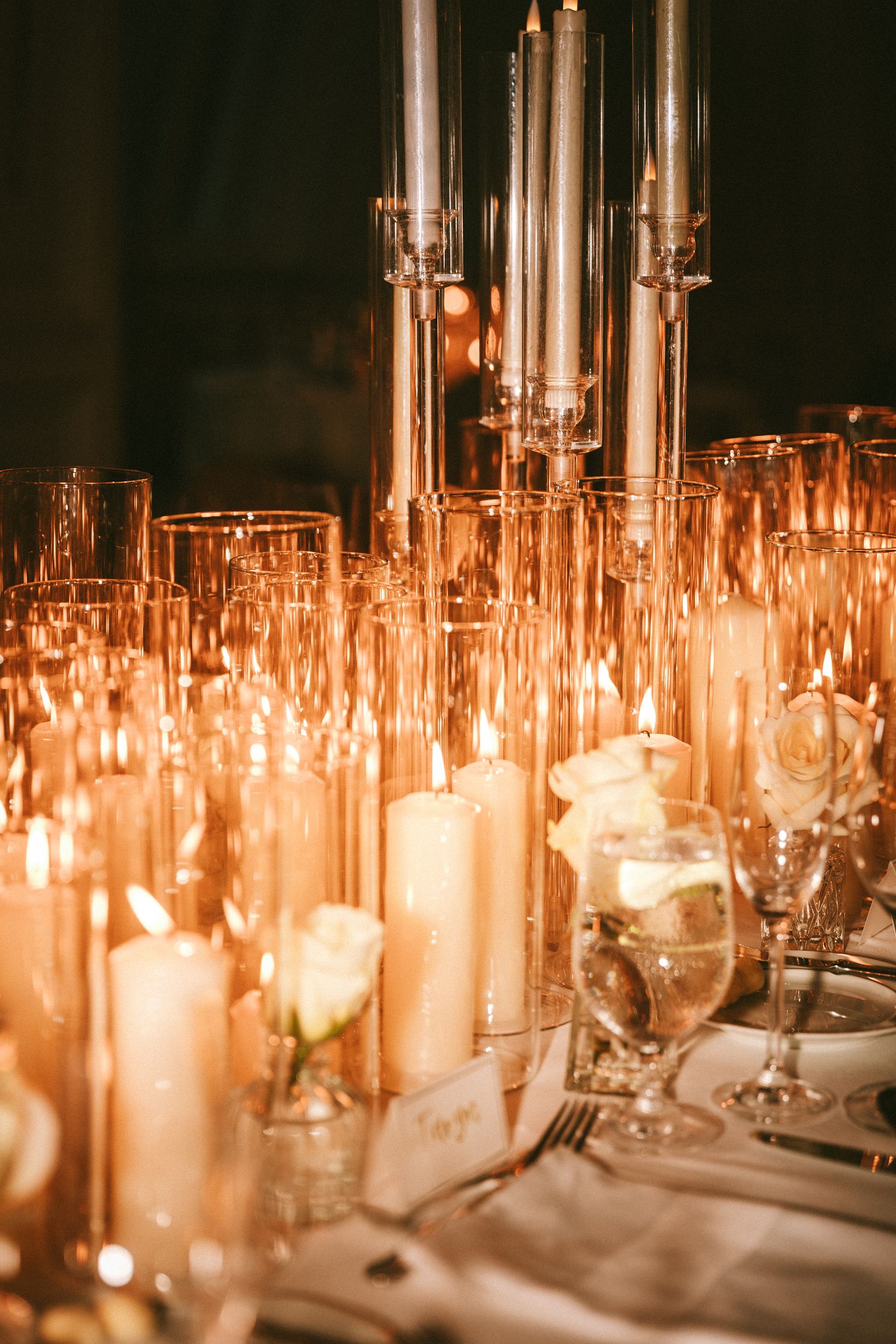 Elegant wedding reception table with glowing candles and crystal glassware centerpiece.