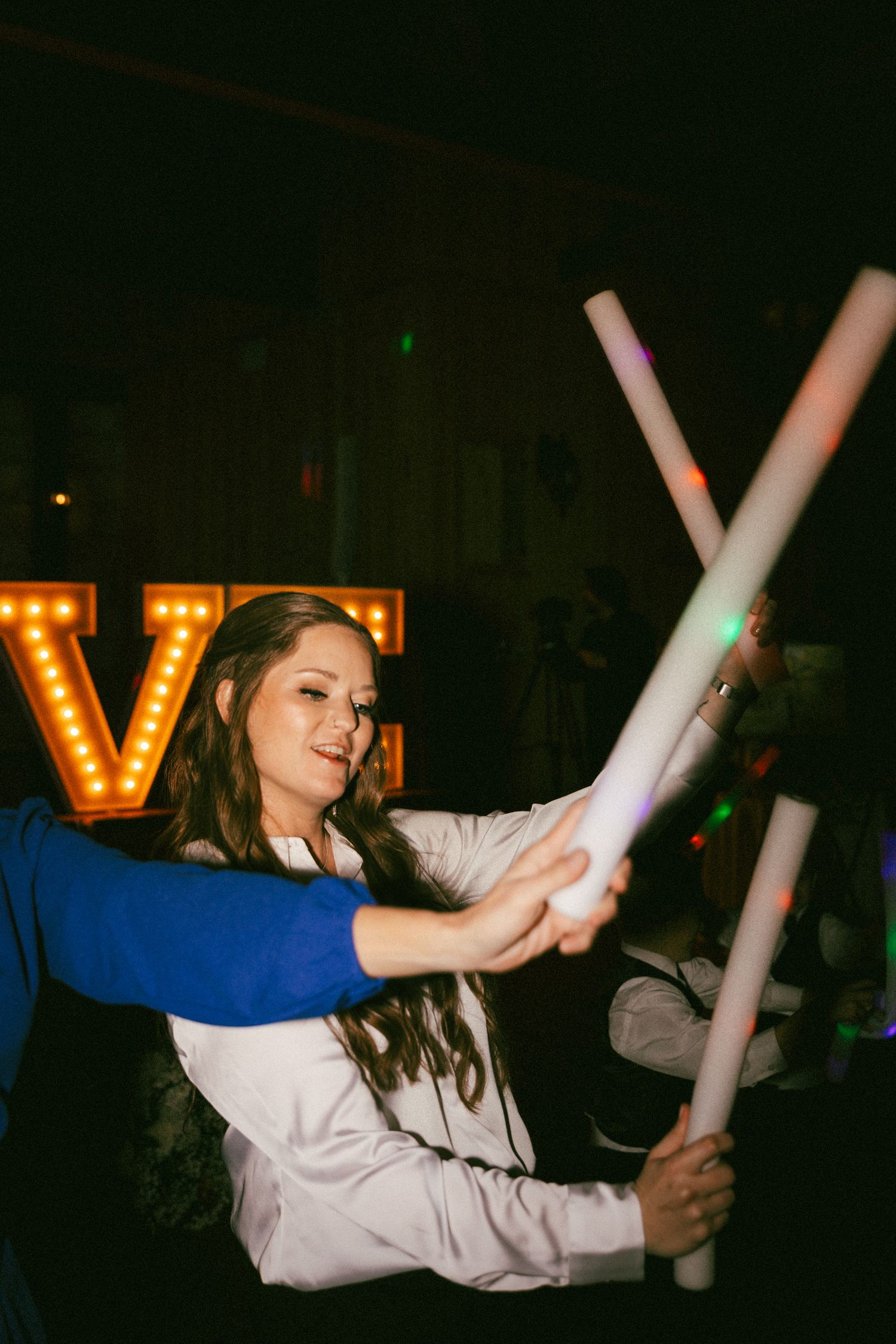 Wedding guest dancing with glowing foam sticks near illuminated LOVE letters at reception.