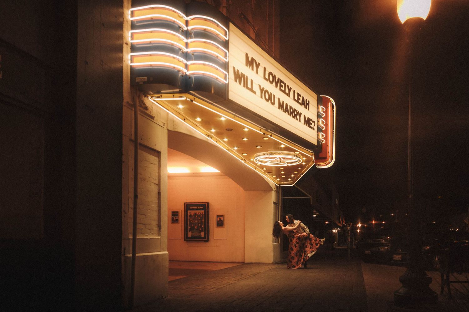 Glowing vintage theater marquee at night displaying a heartfelt marriage proposal message for Leah.