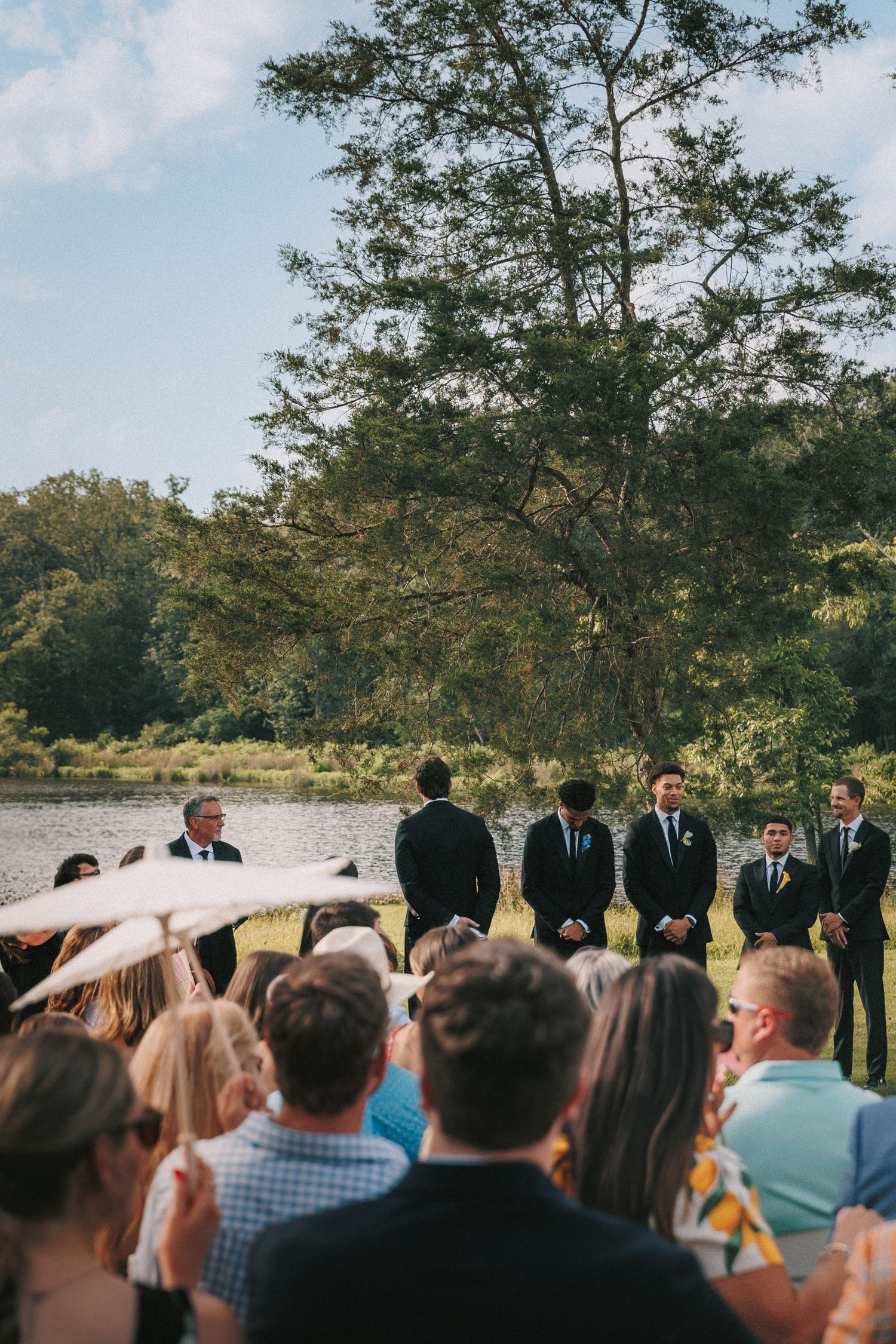 Outdoor wedding ceremony under trees with guests watching the proceedings.