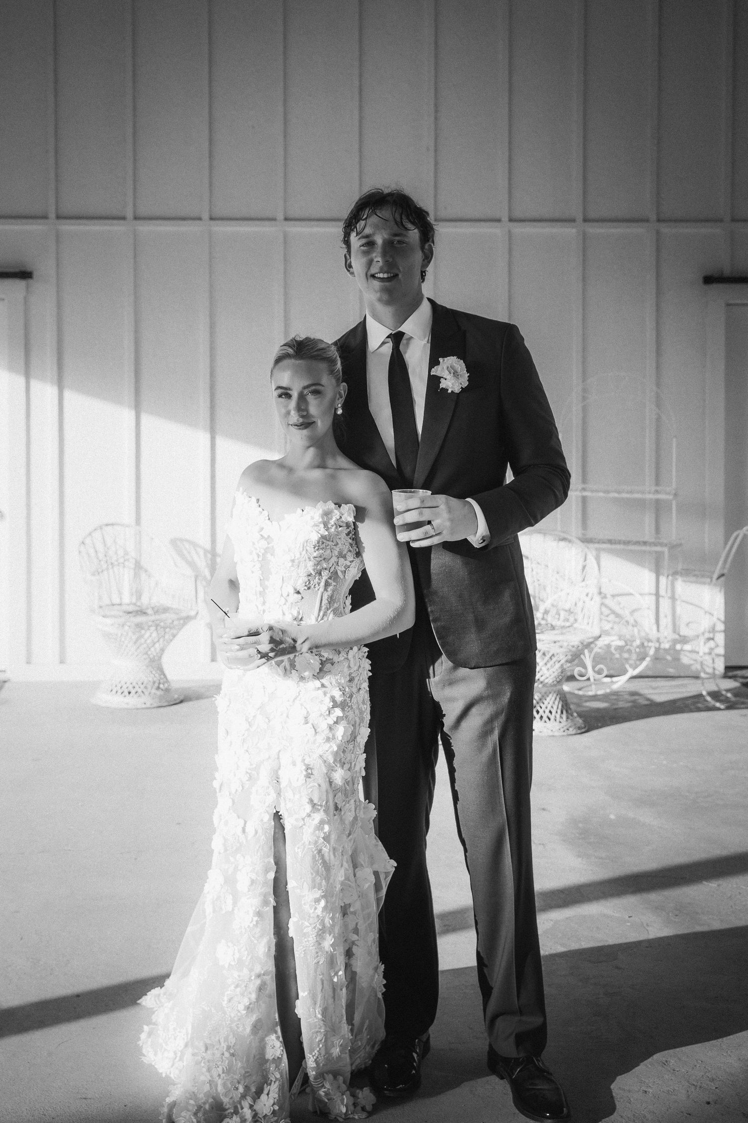 A black and white portrait of a couple in formal wedding attire standing in an elegant venue.