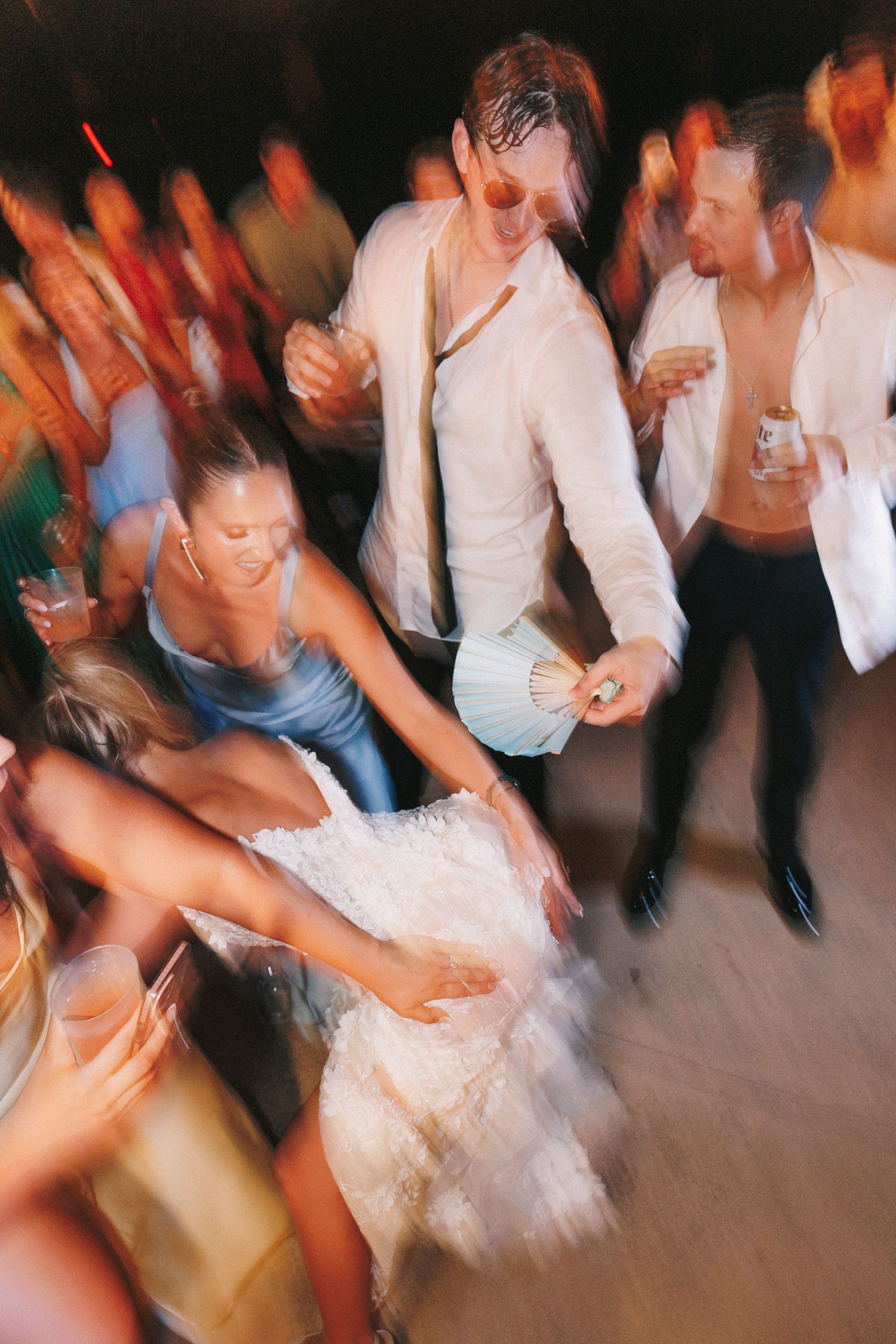Blurred motion shot of wedding guests dancing on the dance floor in white attire.