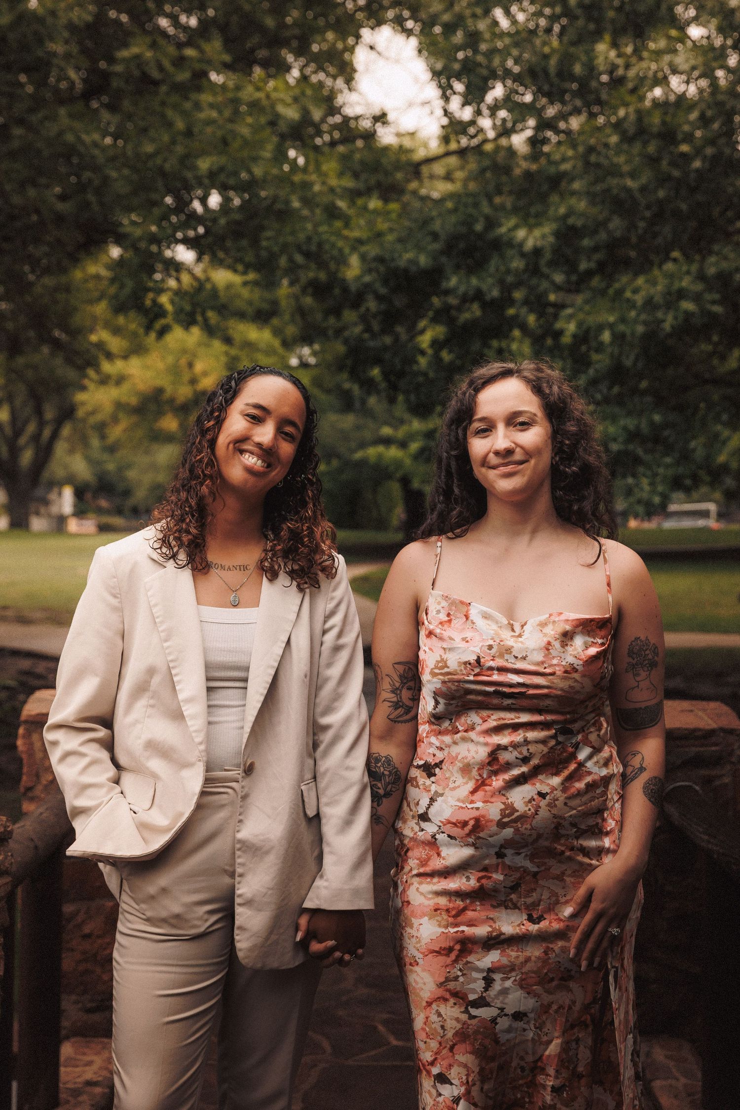 Two people in coordinating beige and floral outfits share joyful moments against a lush green park backdrop.