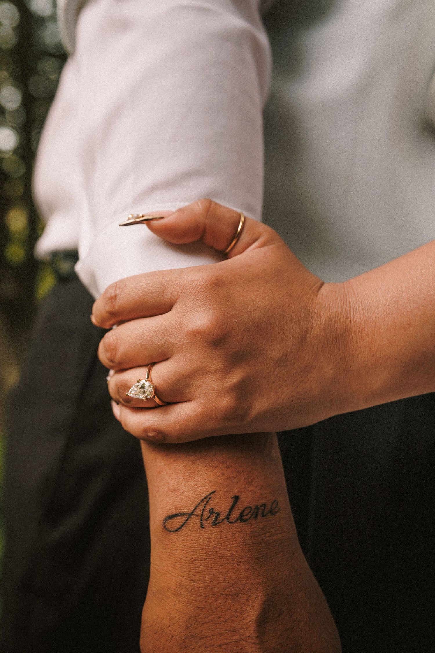 Close-up shots showing hands with engagement ring and cursive tattoo against blurred background.