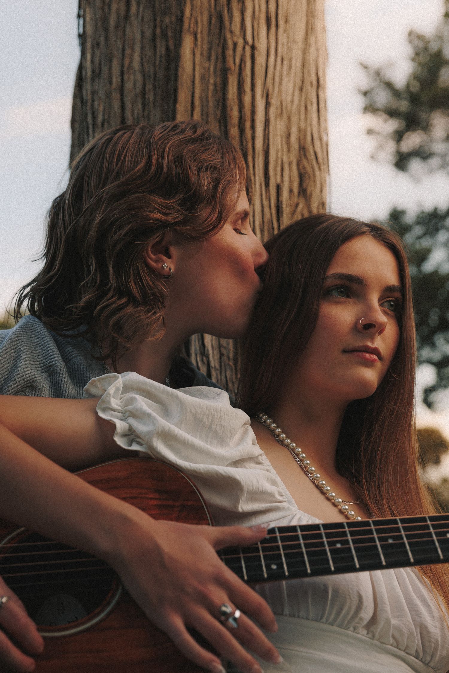 A close-up shot captures an intimate moment with an acoustic guitar and pearl necklace detail.