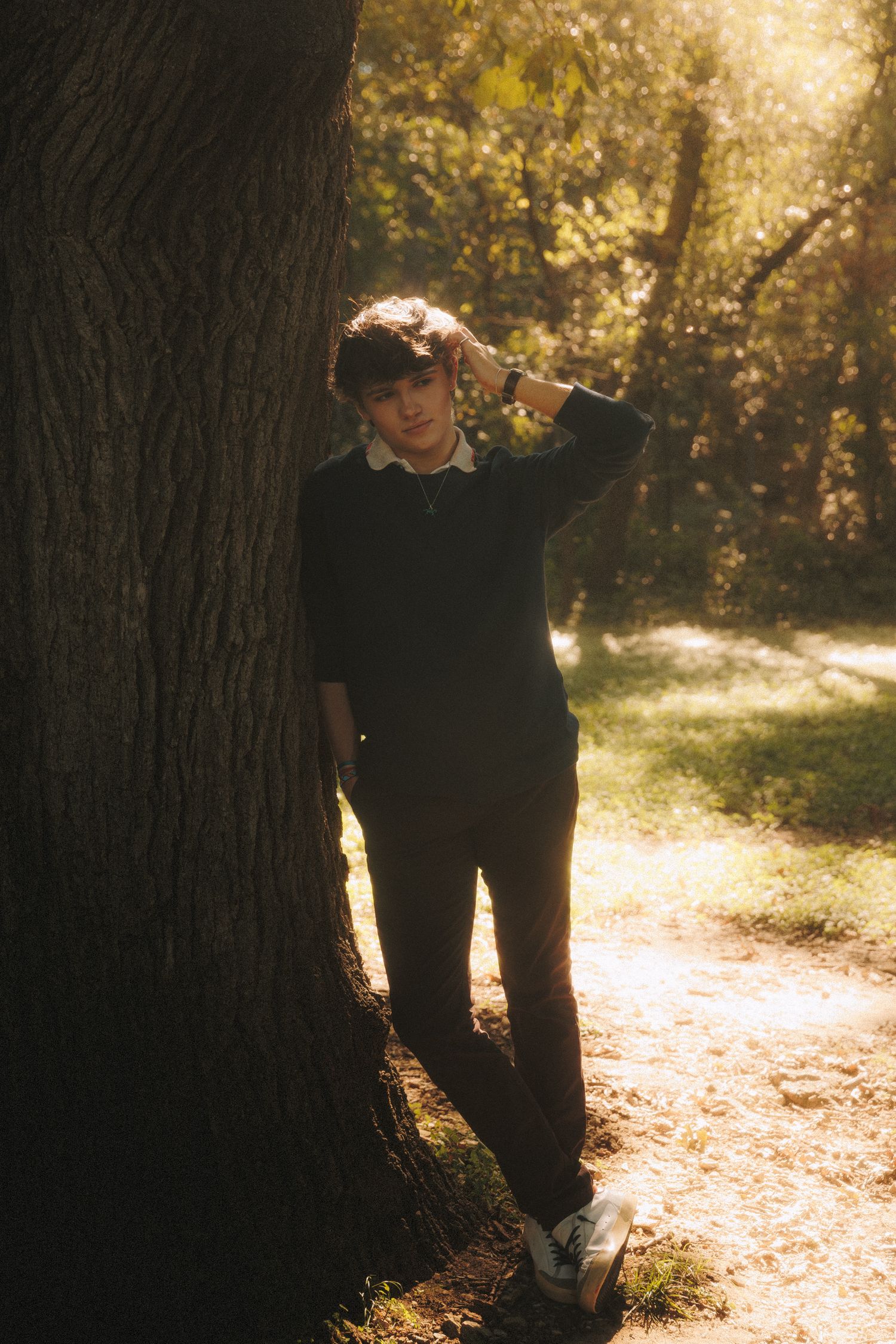 A person stands in silhouette against sunlit trees on a forest path during golden hour.