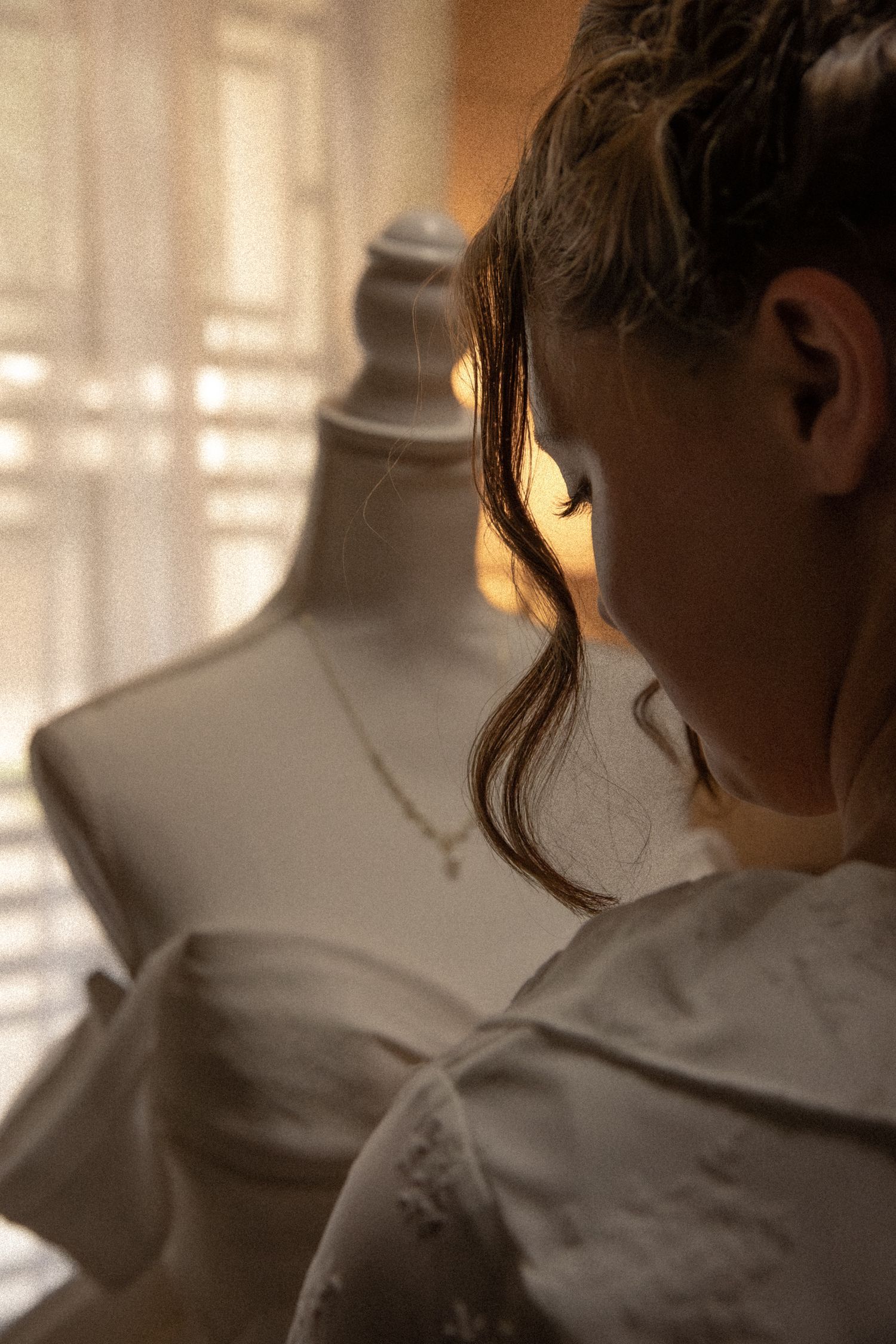 A woman in a white dress stands beside a vintage mannequin bust in warm golden light.