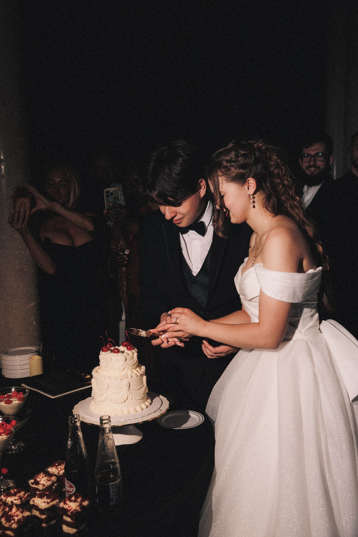 Bride and groom cutting their white wedding cake together at their reception.