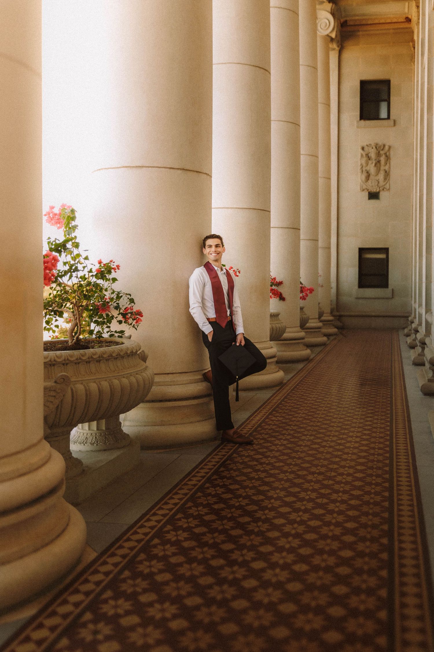 Elegant architectural corridor with white columns, checkerboard floor pattern, and flowering plants creates a grand classical ambiance.