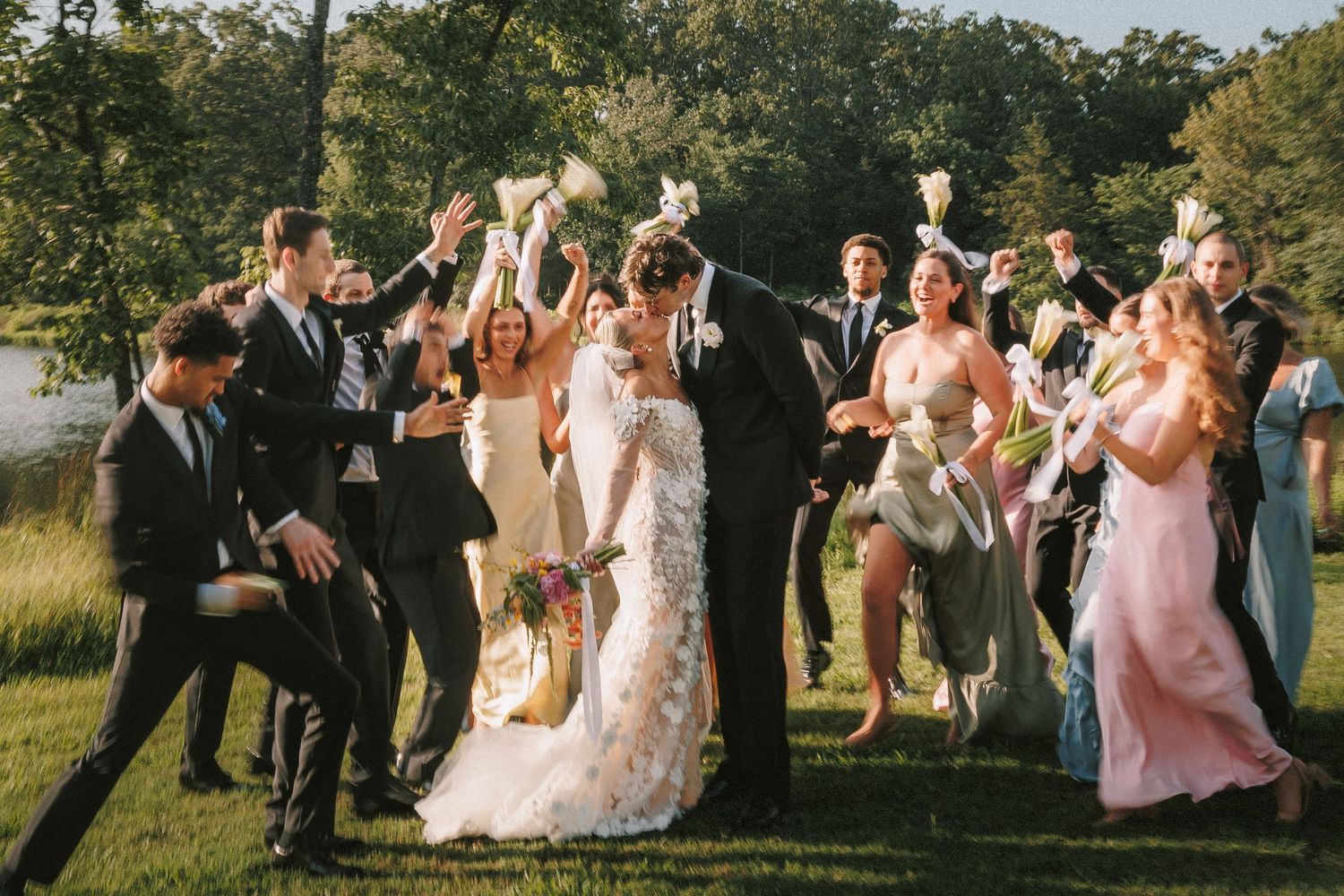 Wedding party celebrates joyfully on sunny outdoor lawn during reception.