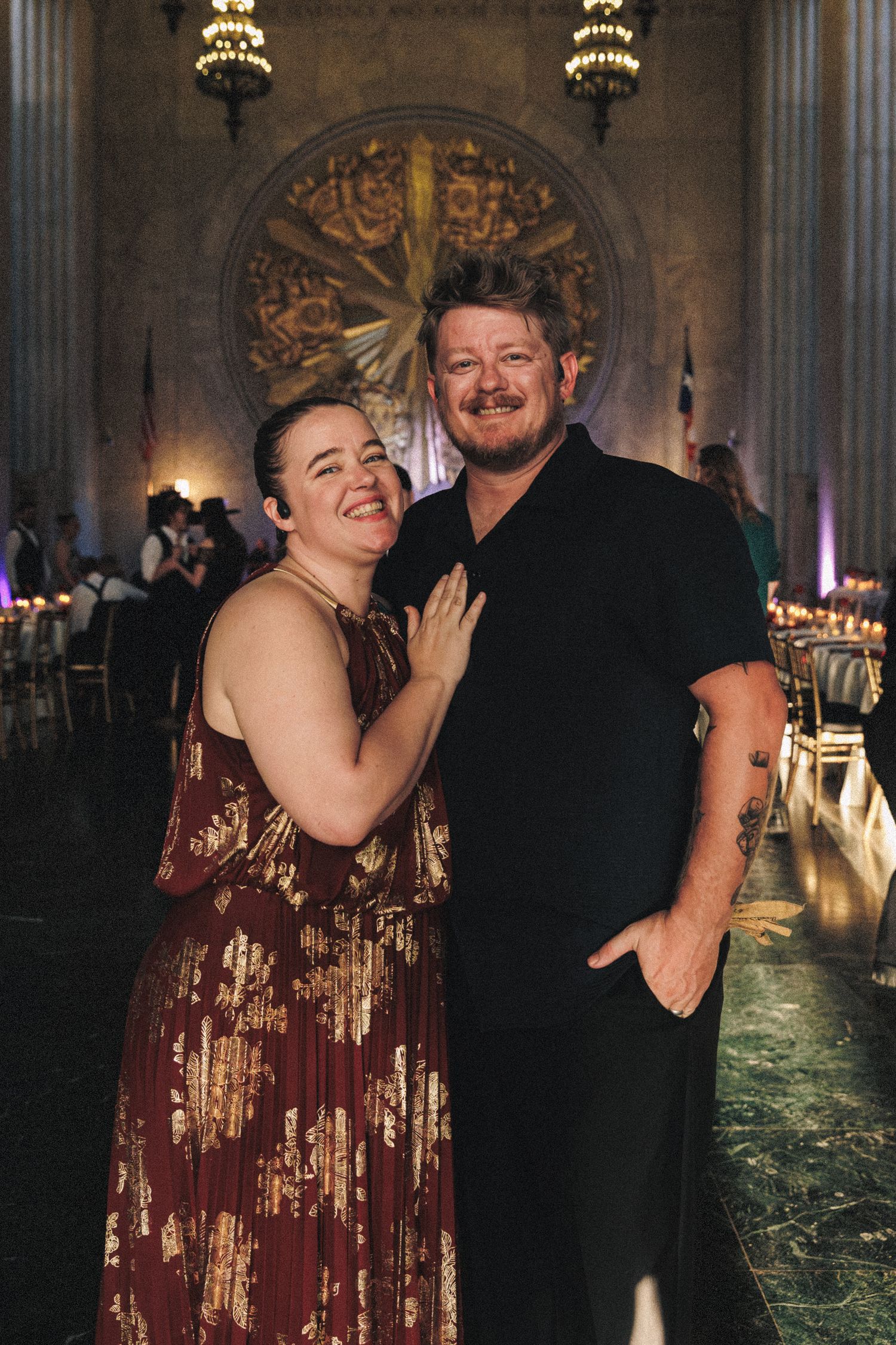 Smiling couple poses together in elegant chandelier-lit wedding reception hall venue.