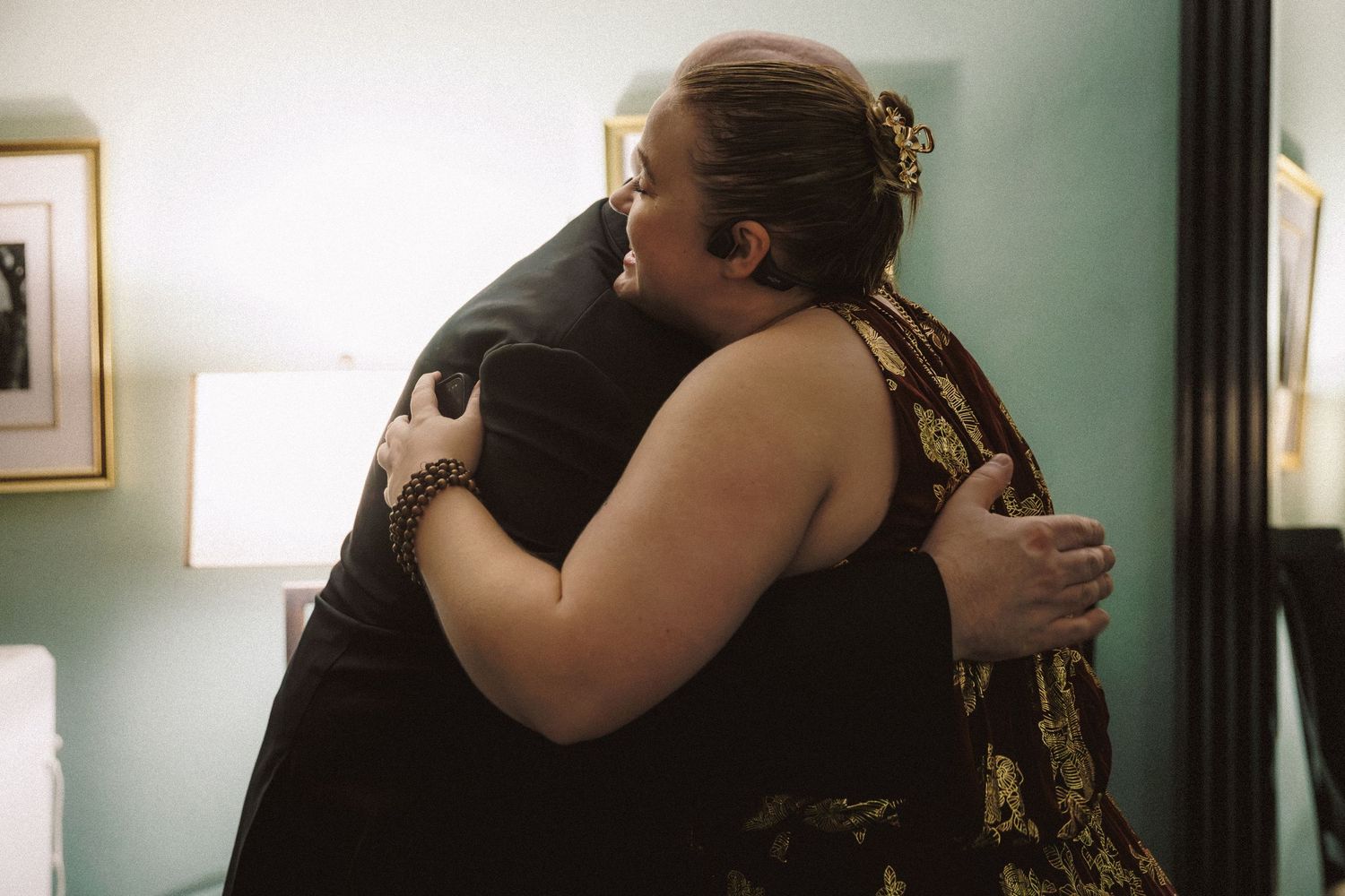 Two women sharing a warm emotional hug during a wedding celebration in a softly lit room.
