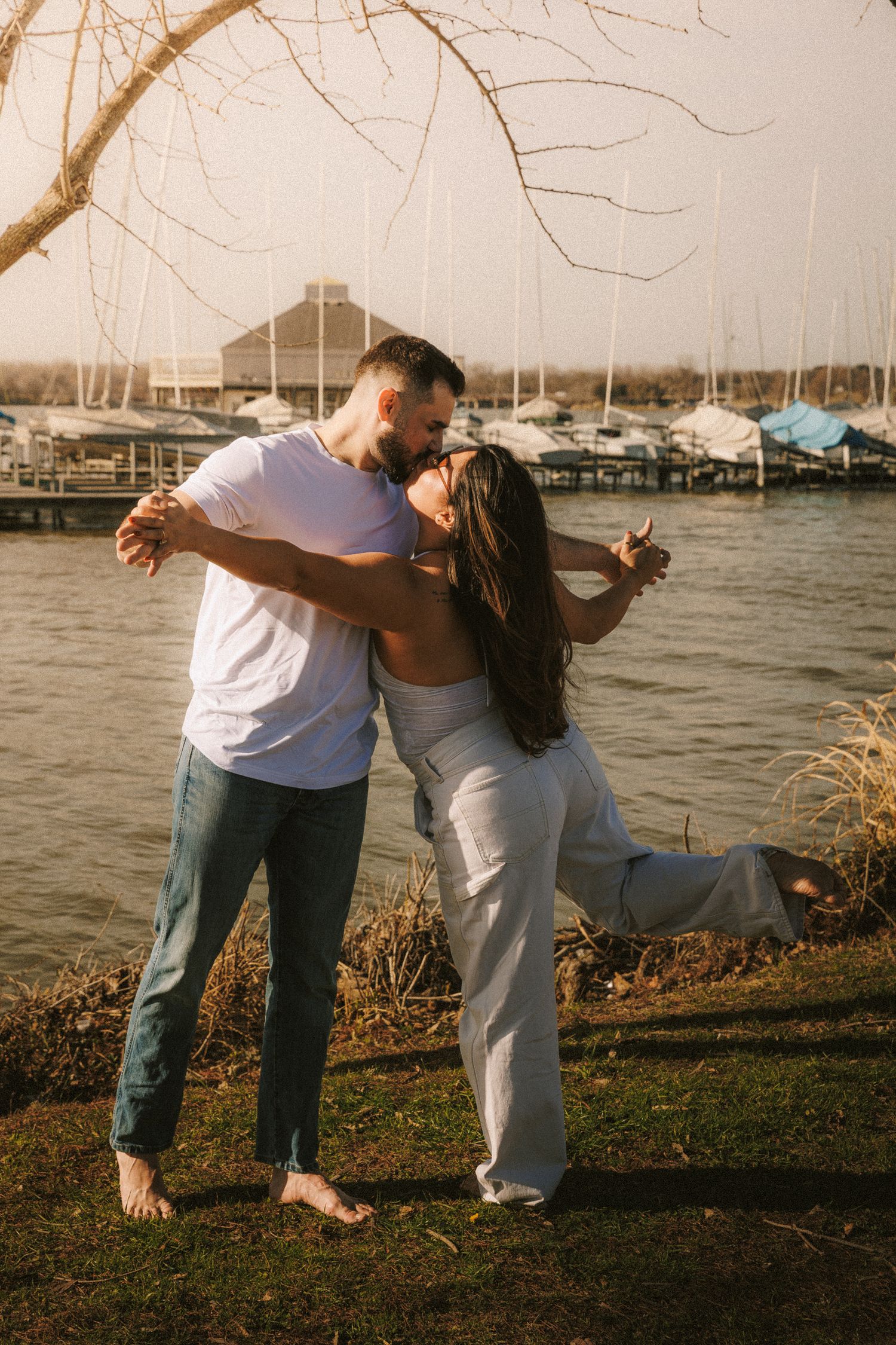 A romantic couple dances playfully together by the waterfront at sunset.