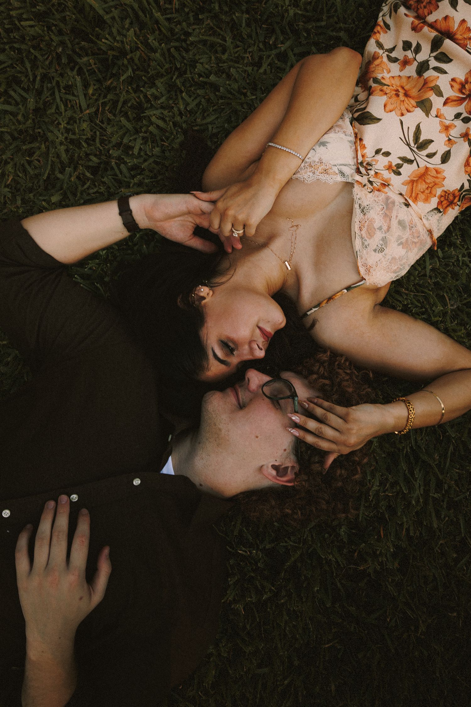 Couple lying on grass sharing intimate moments during sunset photoshoot.