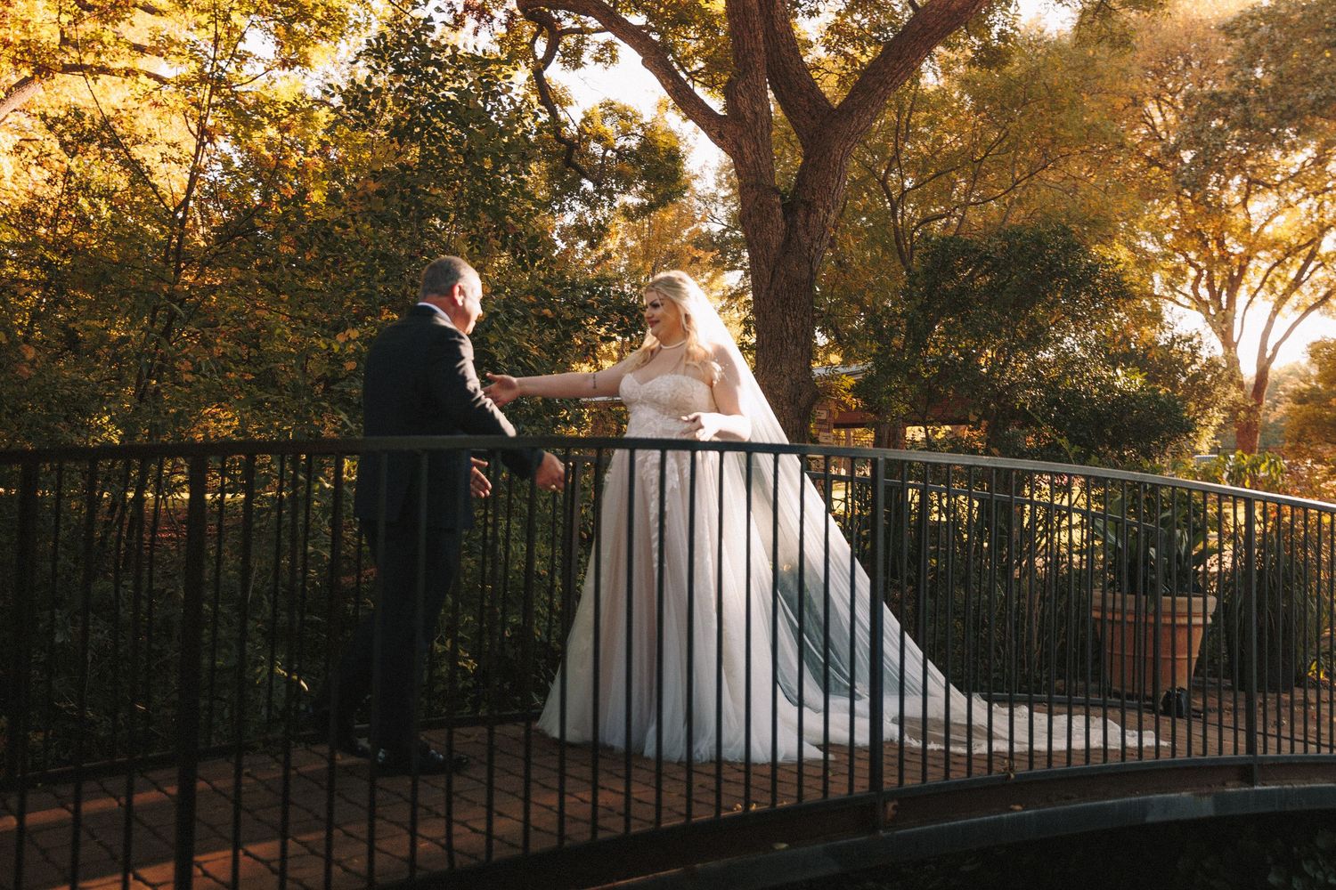 Bride and groom share tender moment on garden bridge surrounded by golden autumn foliage.