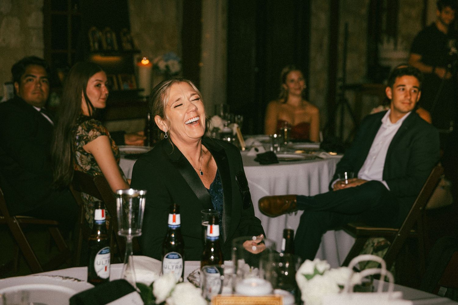 Wedding guest laughing joyfully at candlelit reception table during wedding dinner celebration.