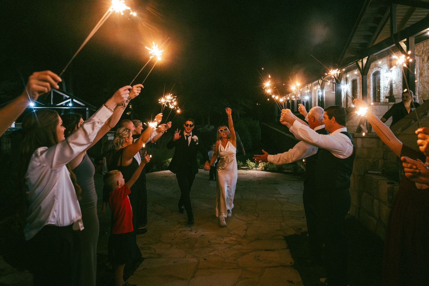 A couple exits through a sparkler tunnel surrounded by cheering guests at their wedding reception.