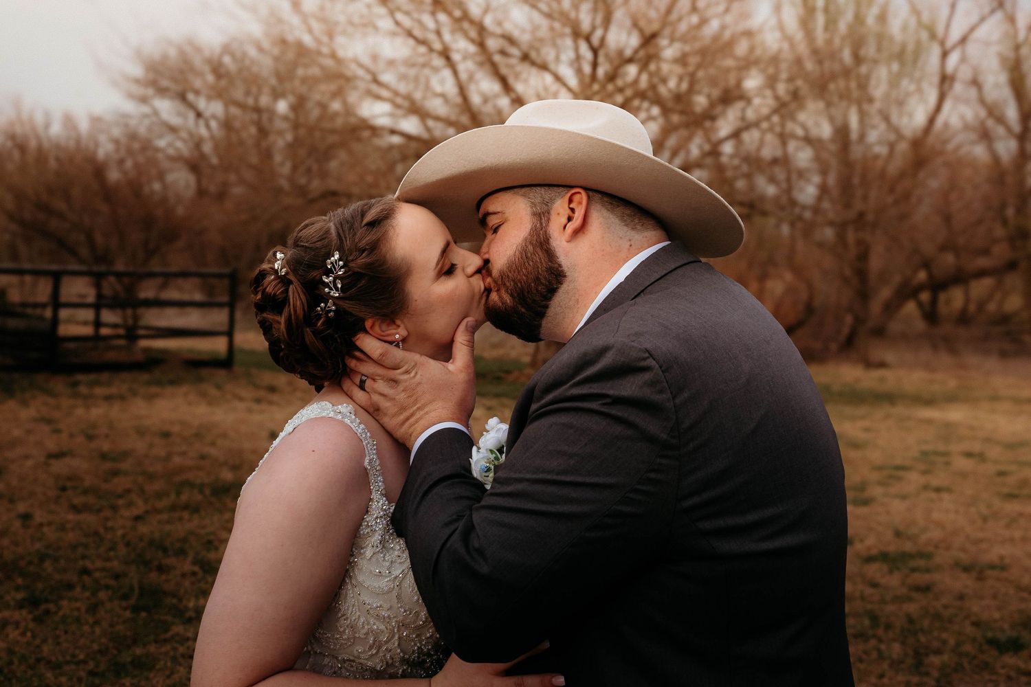 Romantic couple sharing intimate kisses in a dreamy rustic field setting at sunset.
