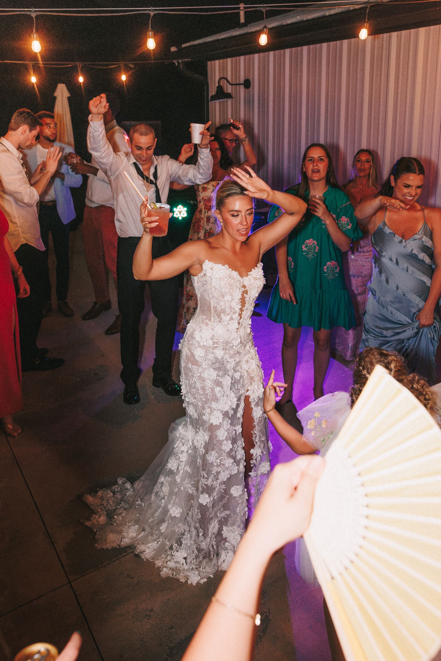 Wedding guests dancing at reception with decorative string lights overhead.