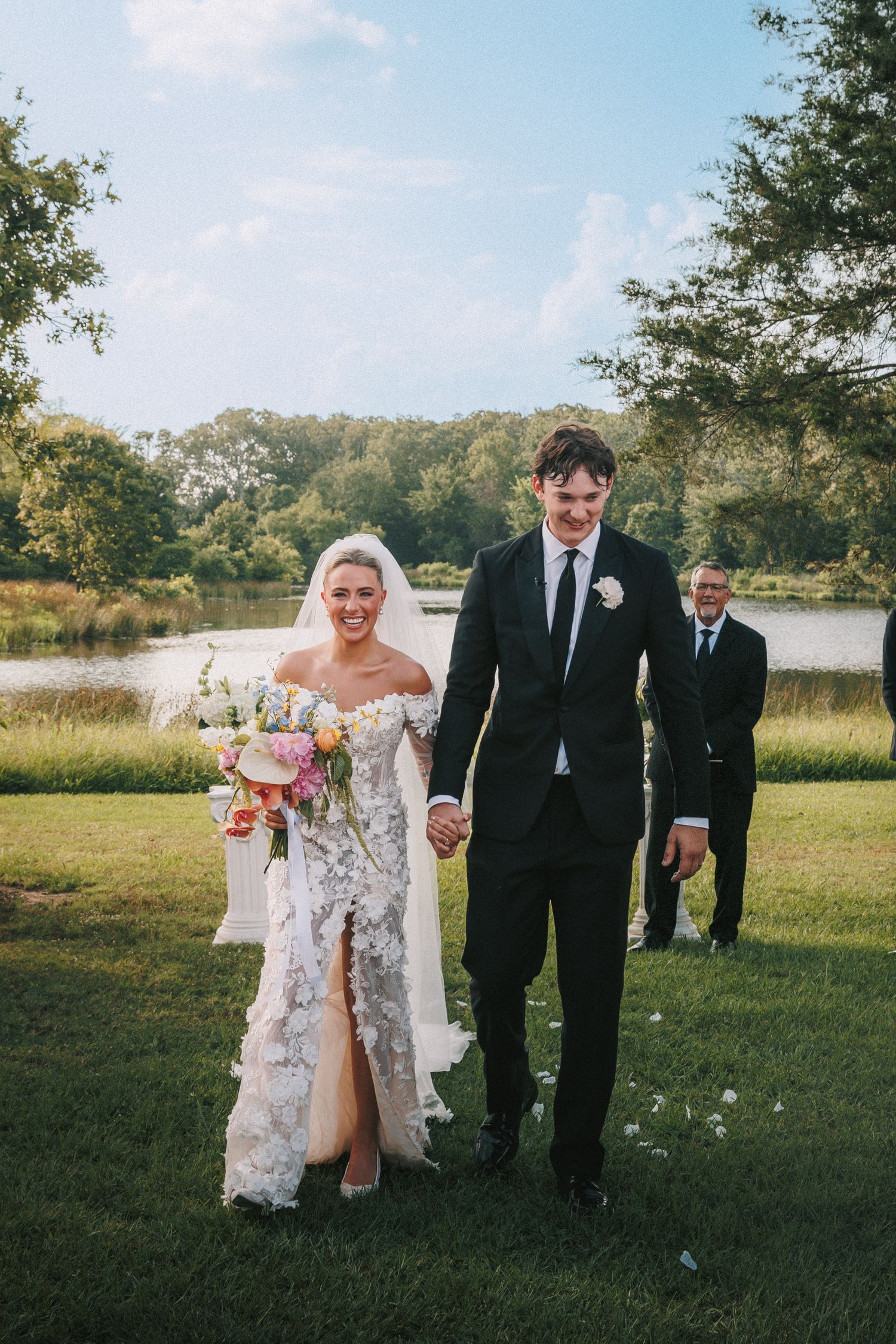 Wedding party members walk together on a grassy lawn during an outdoor ceremony.