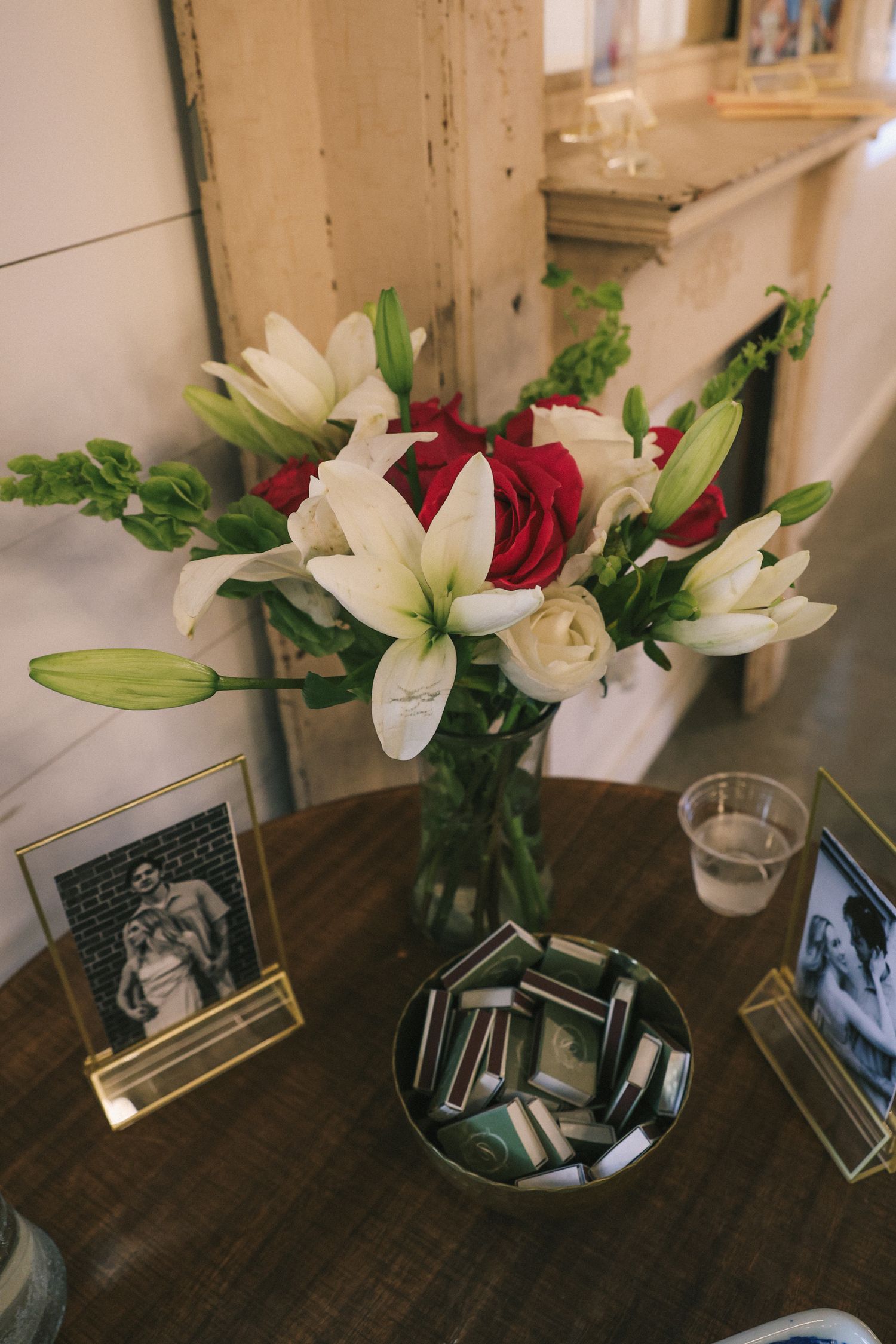 White lilies and red roses in vase displayed with framed photos on dark wooden table.