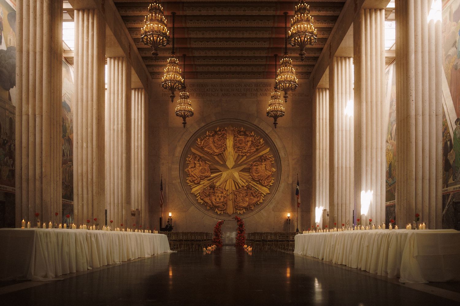 Grand wedding venue hall with ornate chandeliers, tall columns, and decorative golden sunburst medallion.
