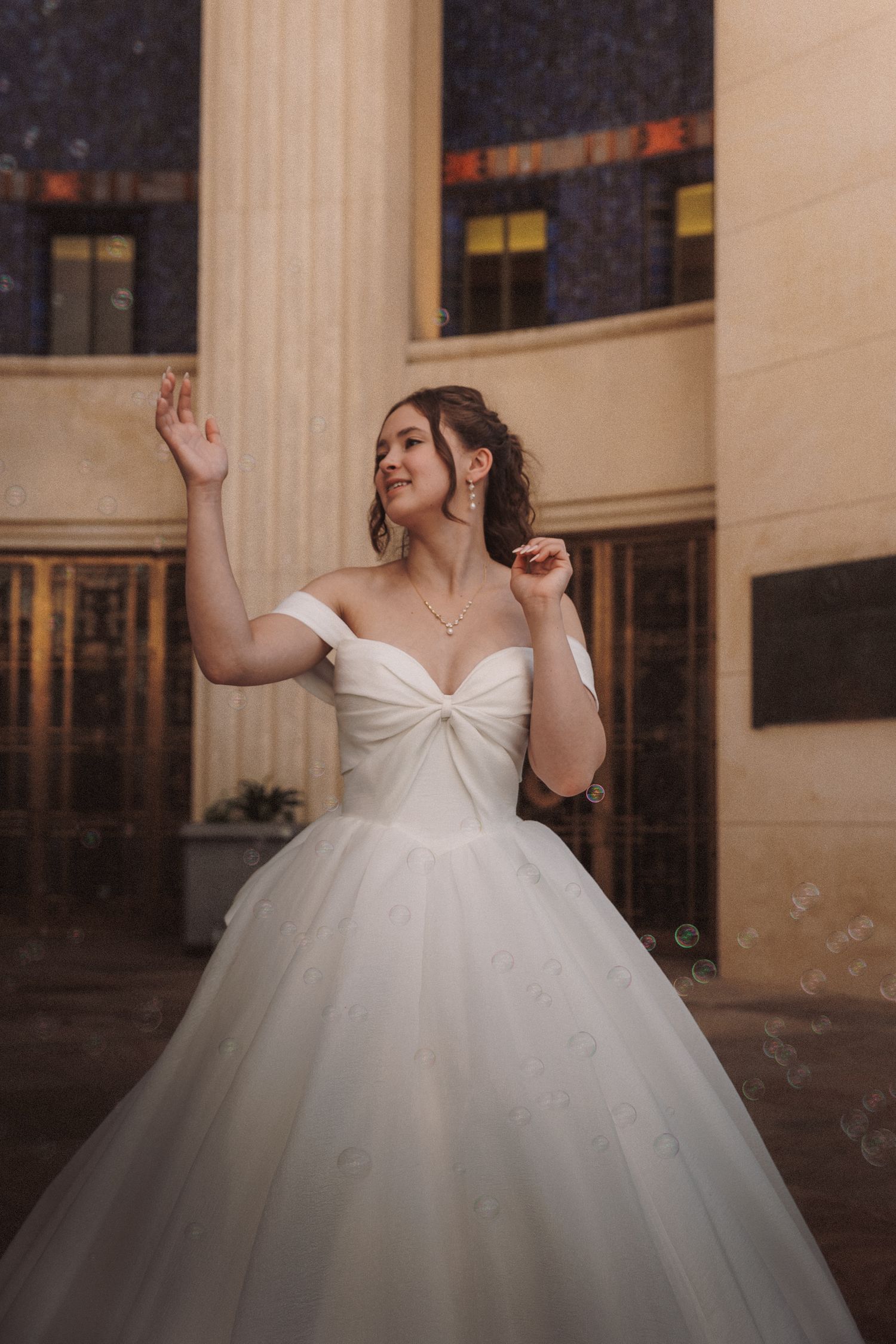 Beautiful bride in an off-shoulder white ball gown posing gracefully in front of grand architectural columns.