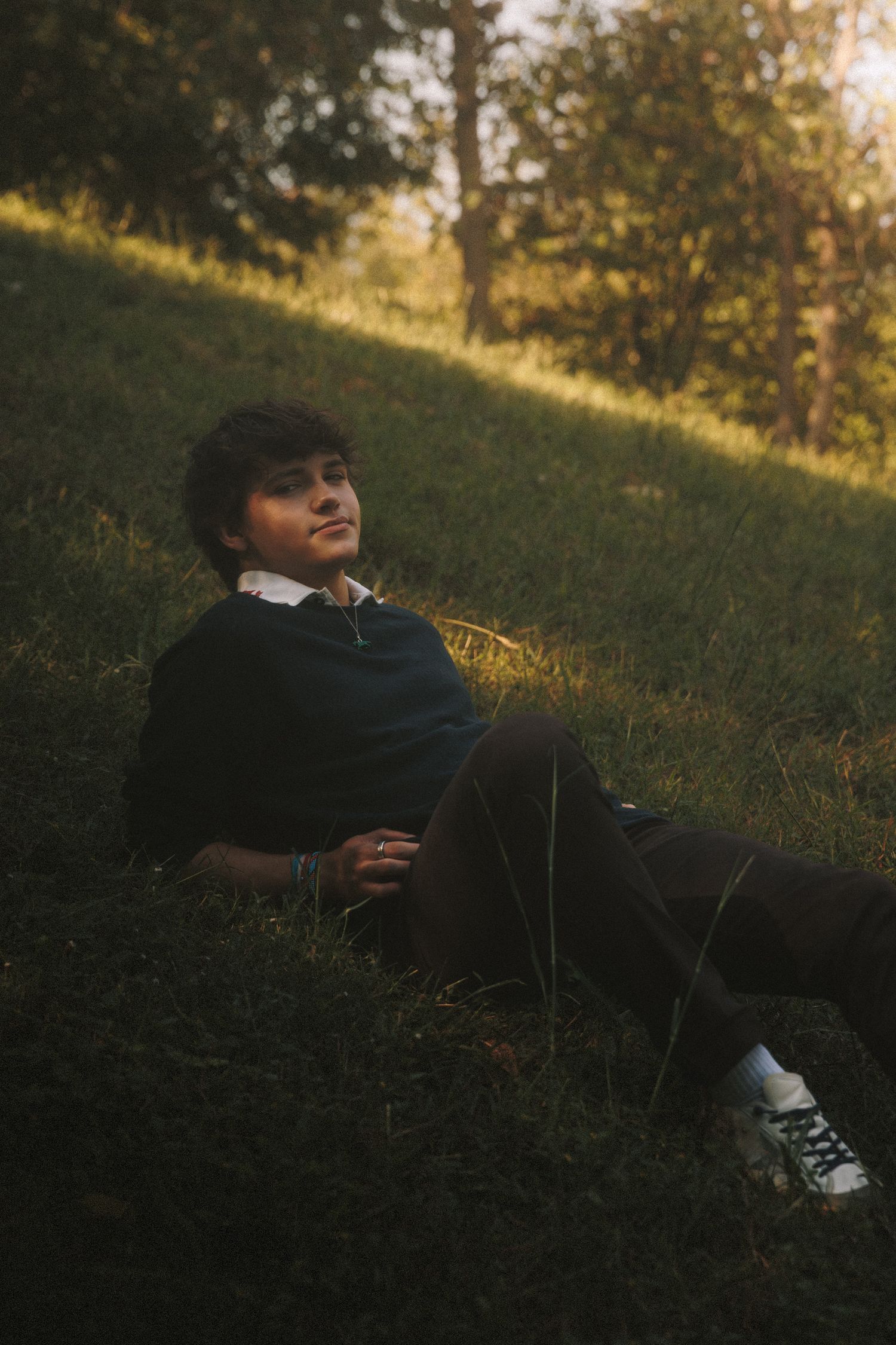 Someone relaxing on a grassy hillside during golden hour with trees in the background.