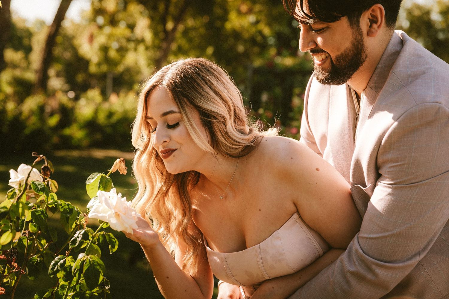 A couple shares a tender moment among blooming garden vines in soft evening light.