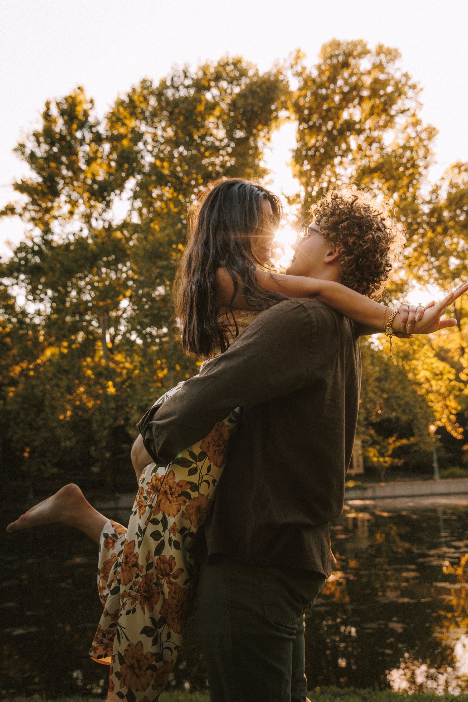 A couple dances together in front of trees during a golden sunset.