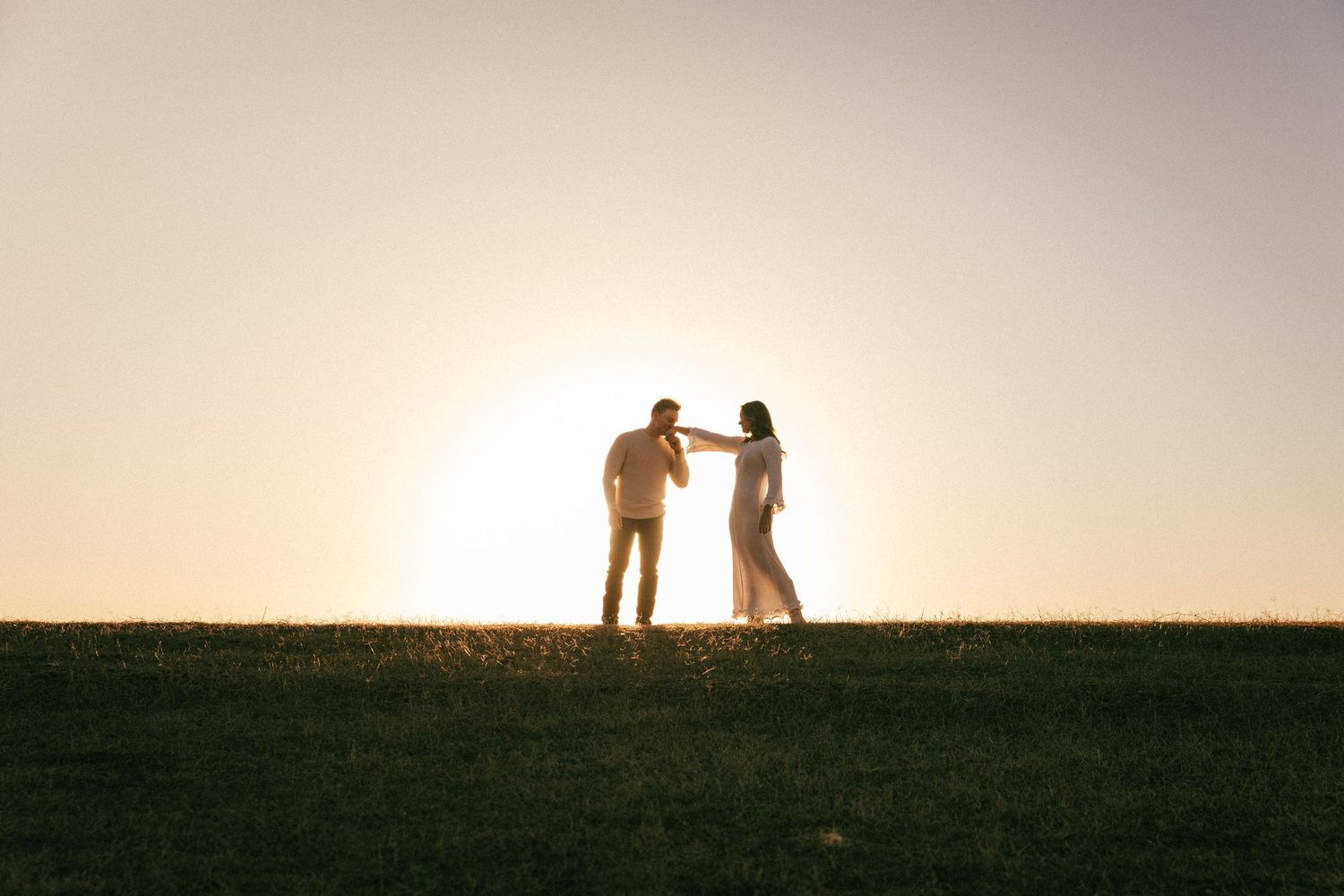 Silhouettes of figures standing on a hill against a warm golden sunset backdrop.
