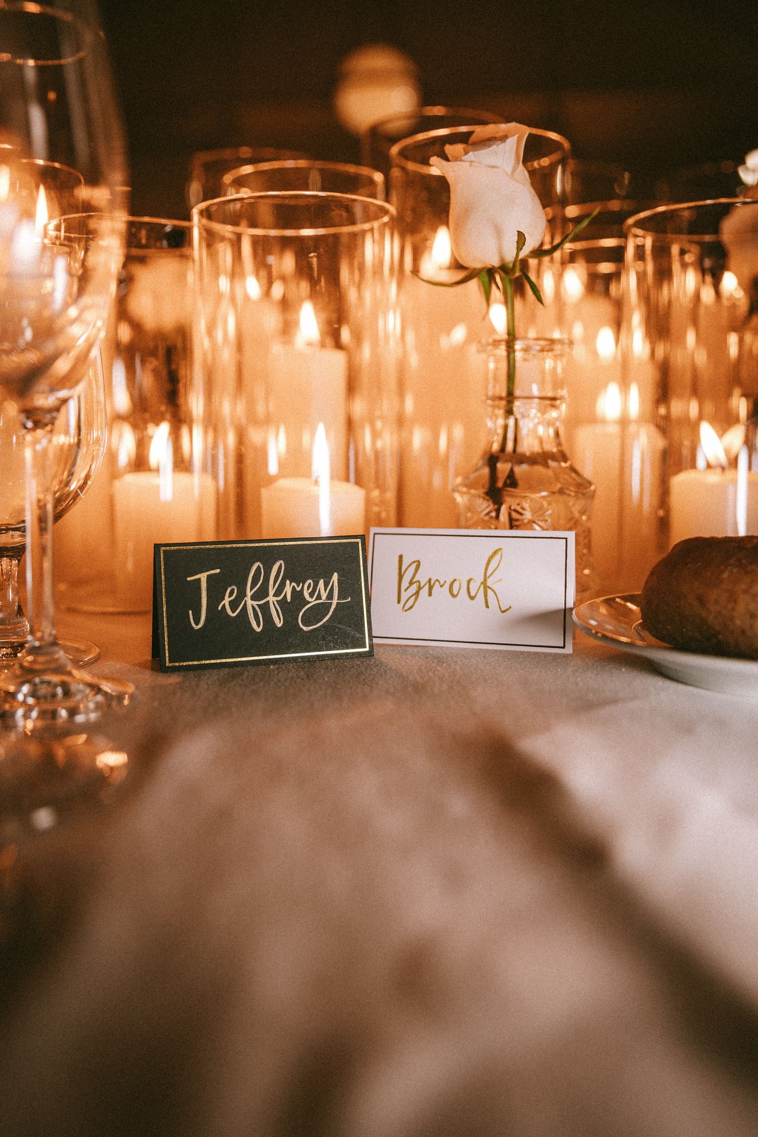 Elegant wedding place cards for Jeffrey and Brock surrounded by glowing candles at reception table.