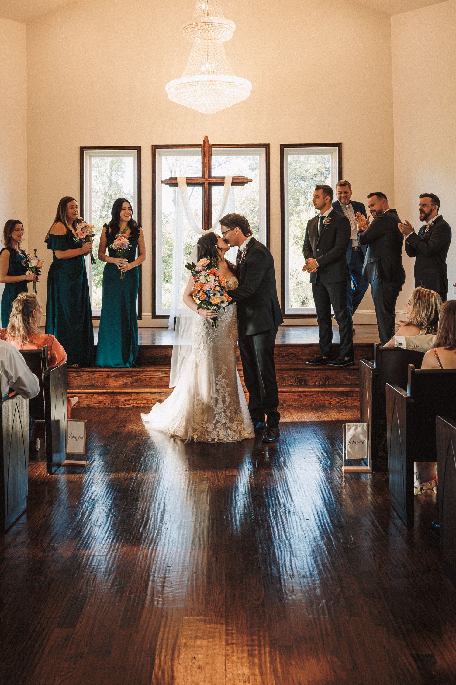 Bride and groom sharing a romantic kiss at the chapel entrance with bridesmaids and groomsmen nearby.