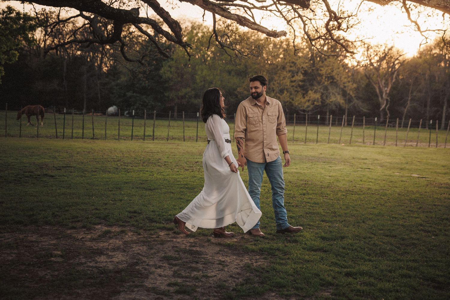 Couple holding hands walking through a sunlit green pasture on a farm.
