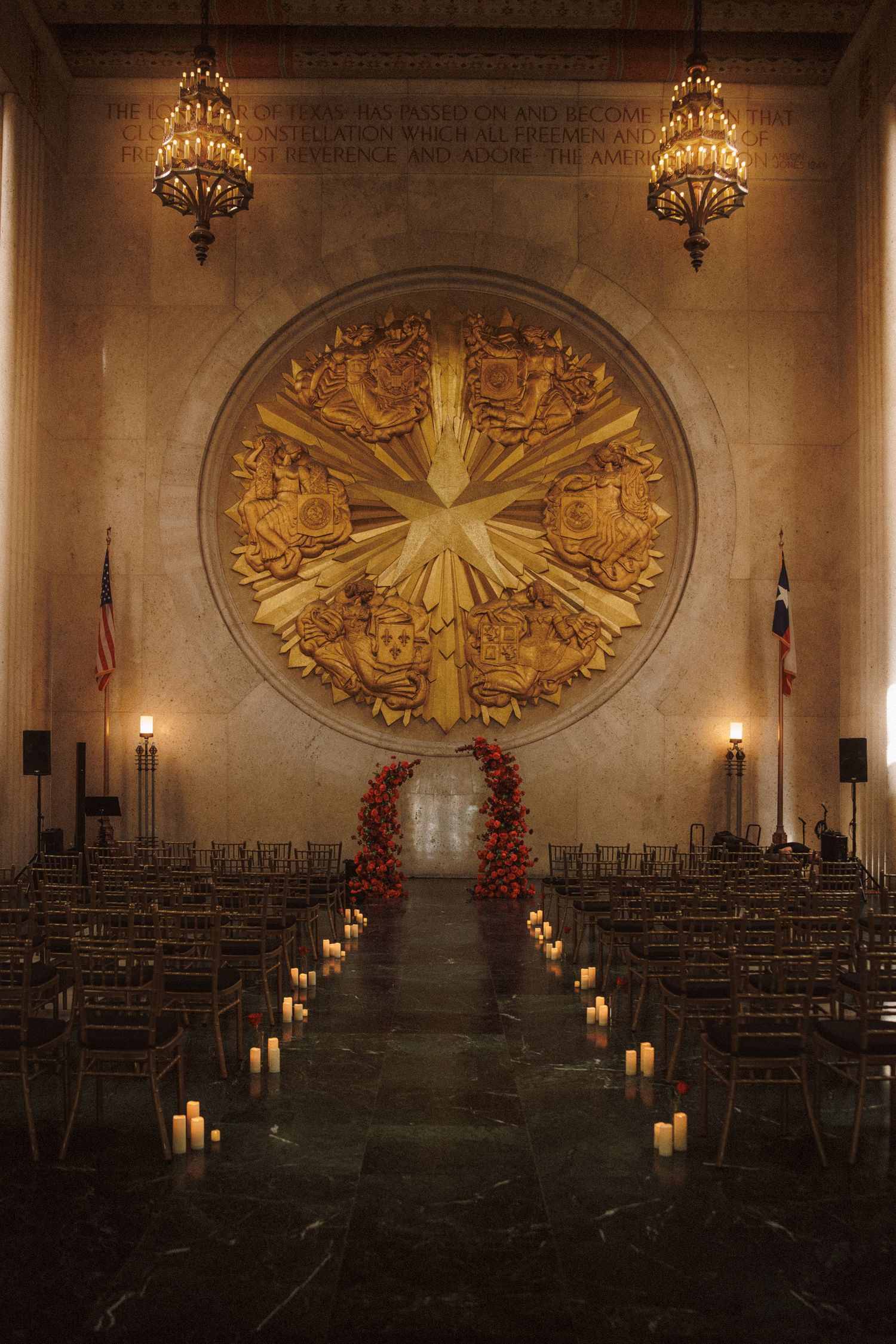 Elegant wedding ceremony hall with golden circular mural, candle-lined aisle, and floral arch in historic venue.