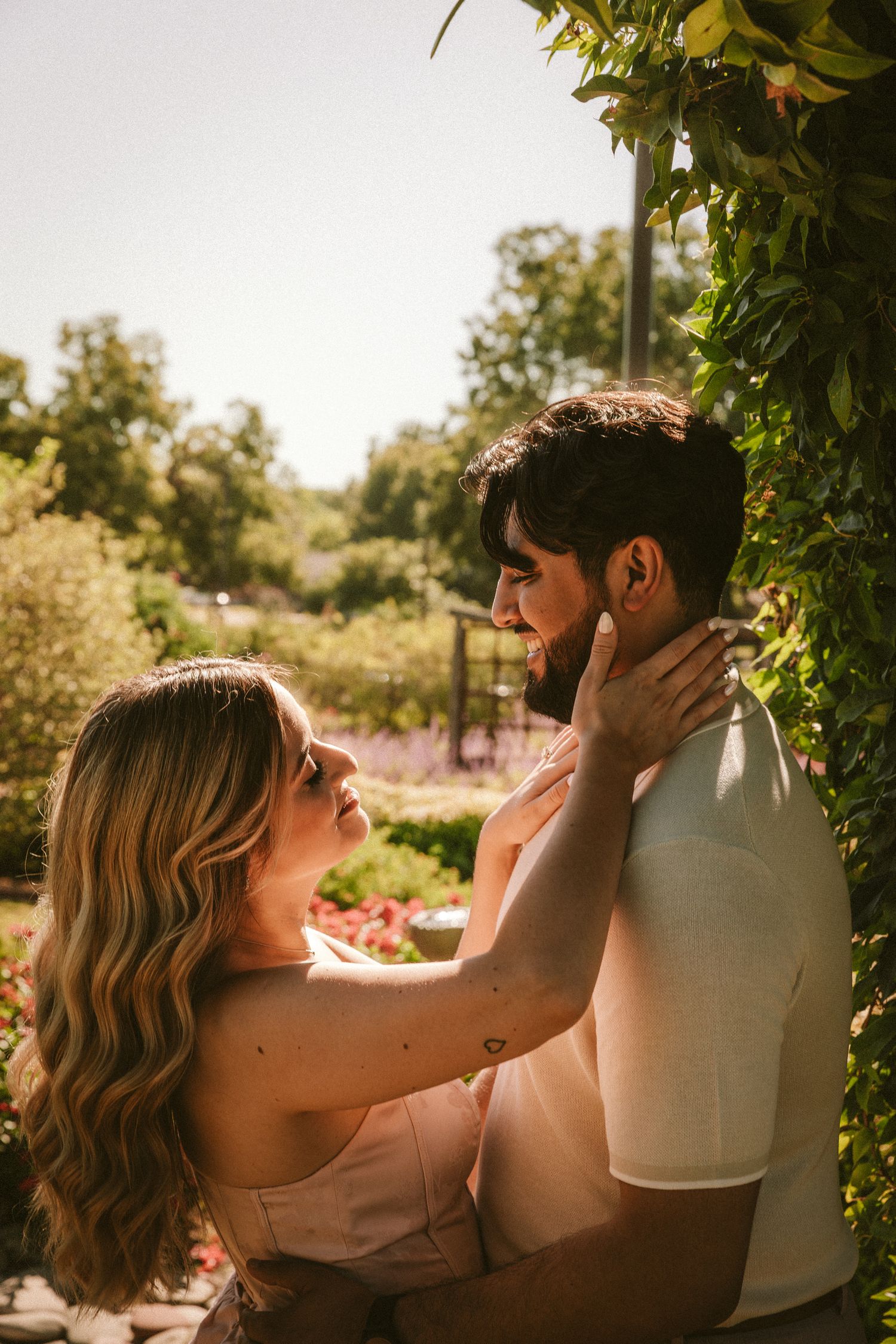 An intimate portrait of a couple embracing against a backdrop of green foliage in warm sunlight.