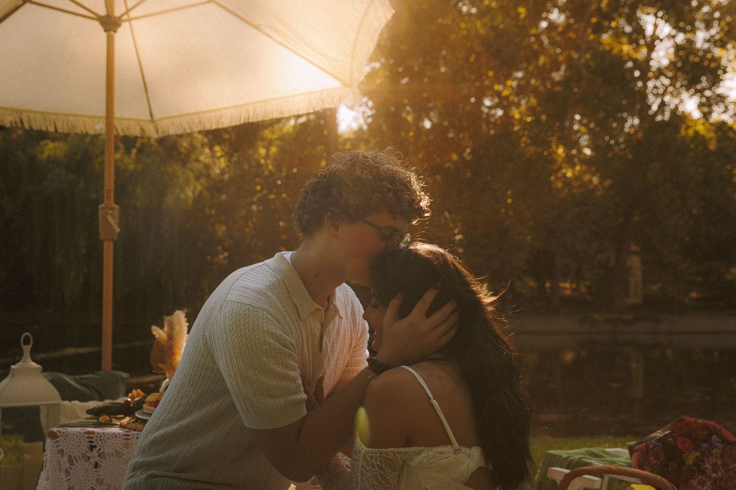 Romantic couple sharing tender moments at sunset in a park setting with golden light filtering through trees.