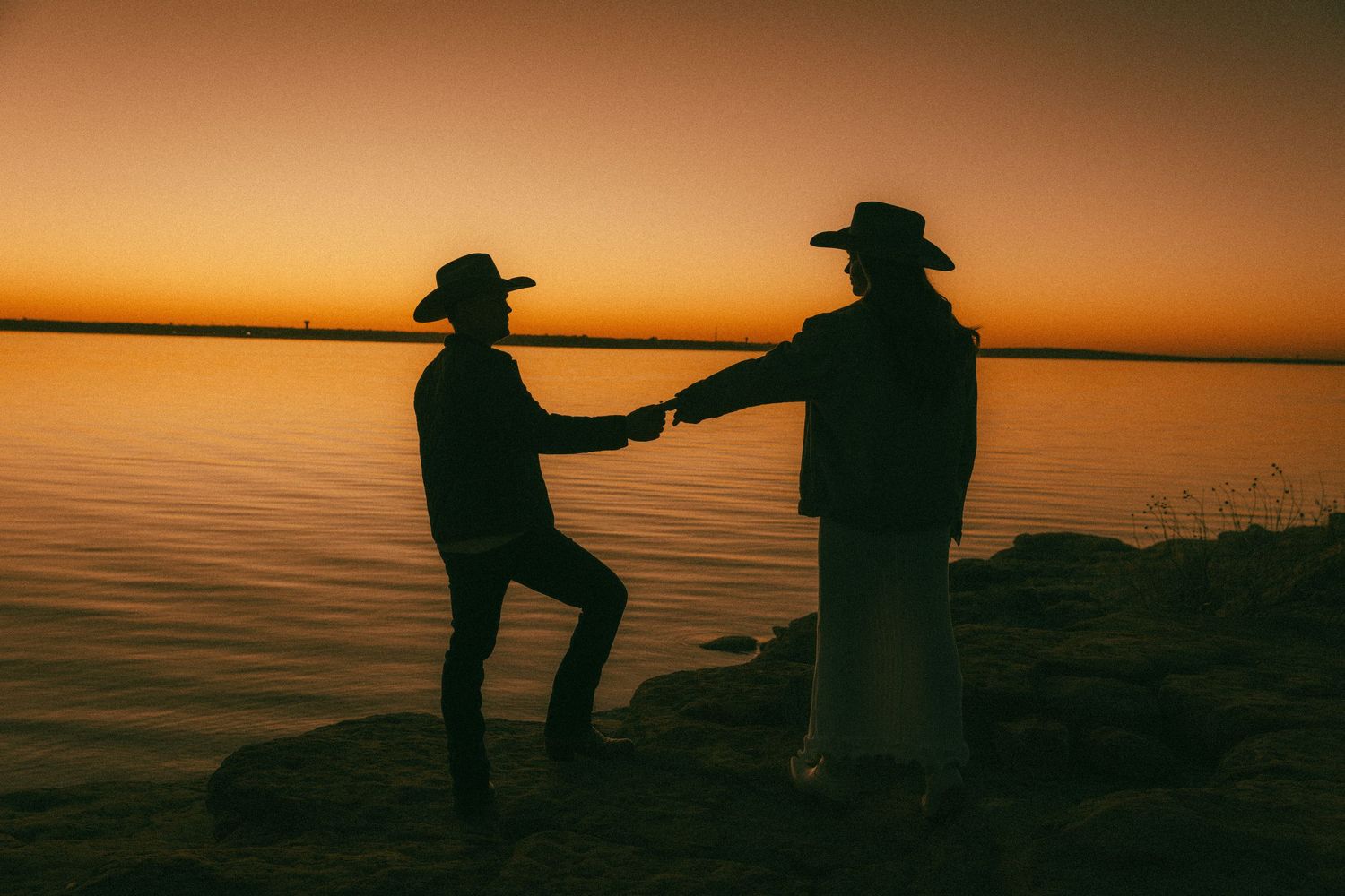 Silhouettes dancing against vibrant orange sunset sky.