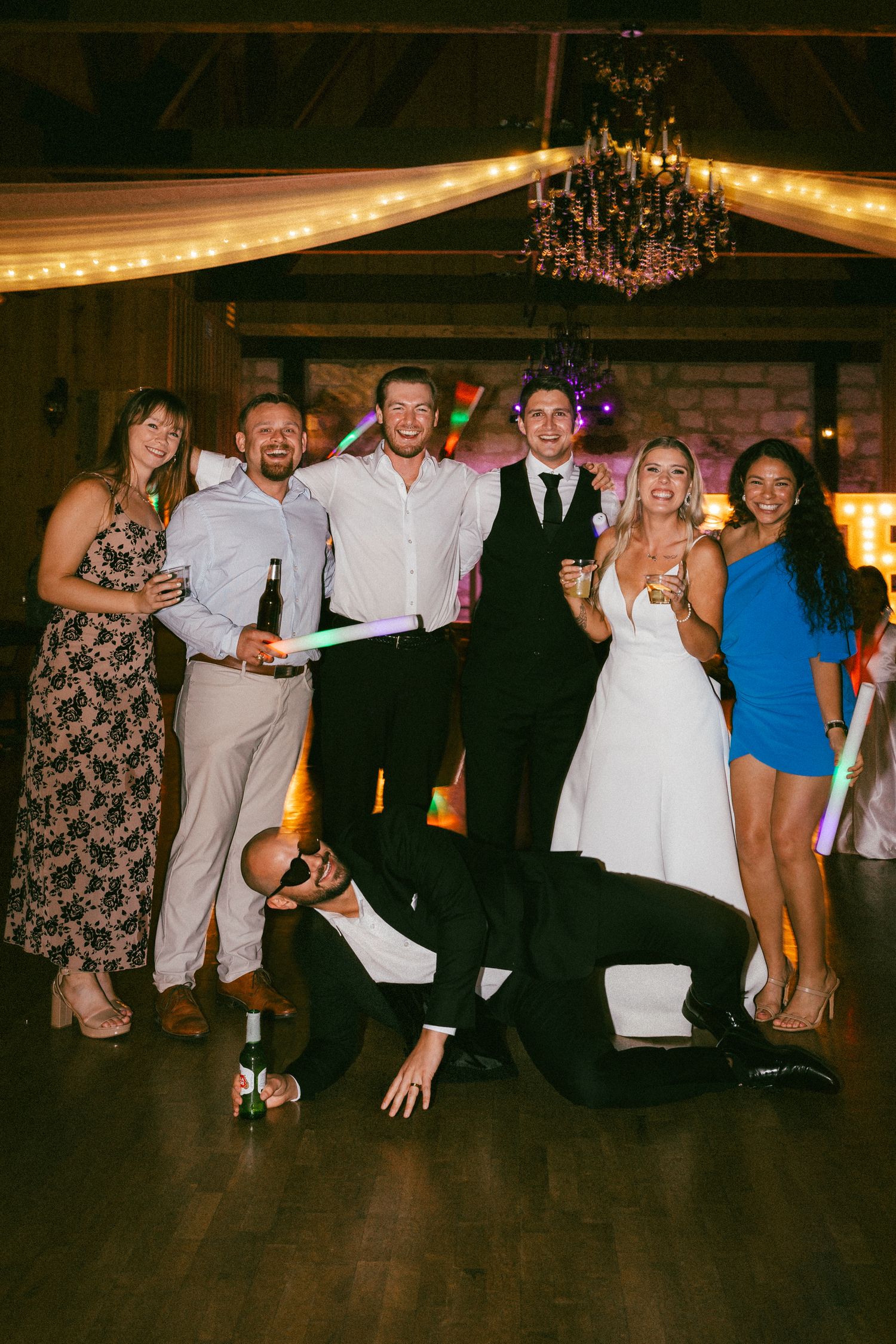 Bride and groom celebrate with friends on a decorated dance floor with glow sticks at reception.
