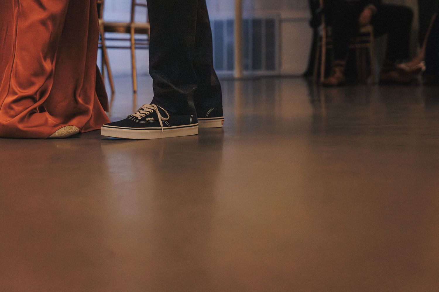 Close-up of a person wearing black Vans sneakers on a polished floor at a wedding reception.