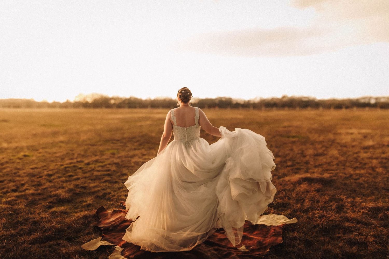 Bride in a flowing white dress runs through a golden field at sunset creating a dreamy silhouette.
