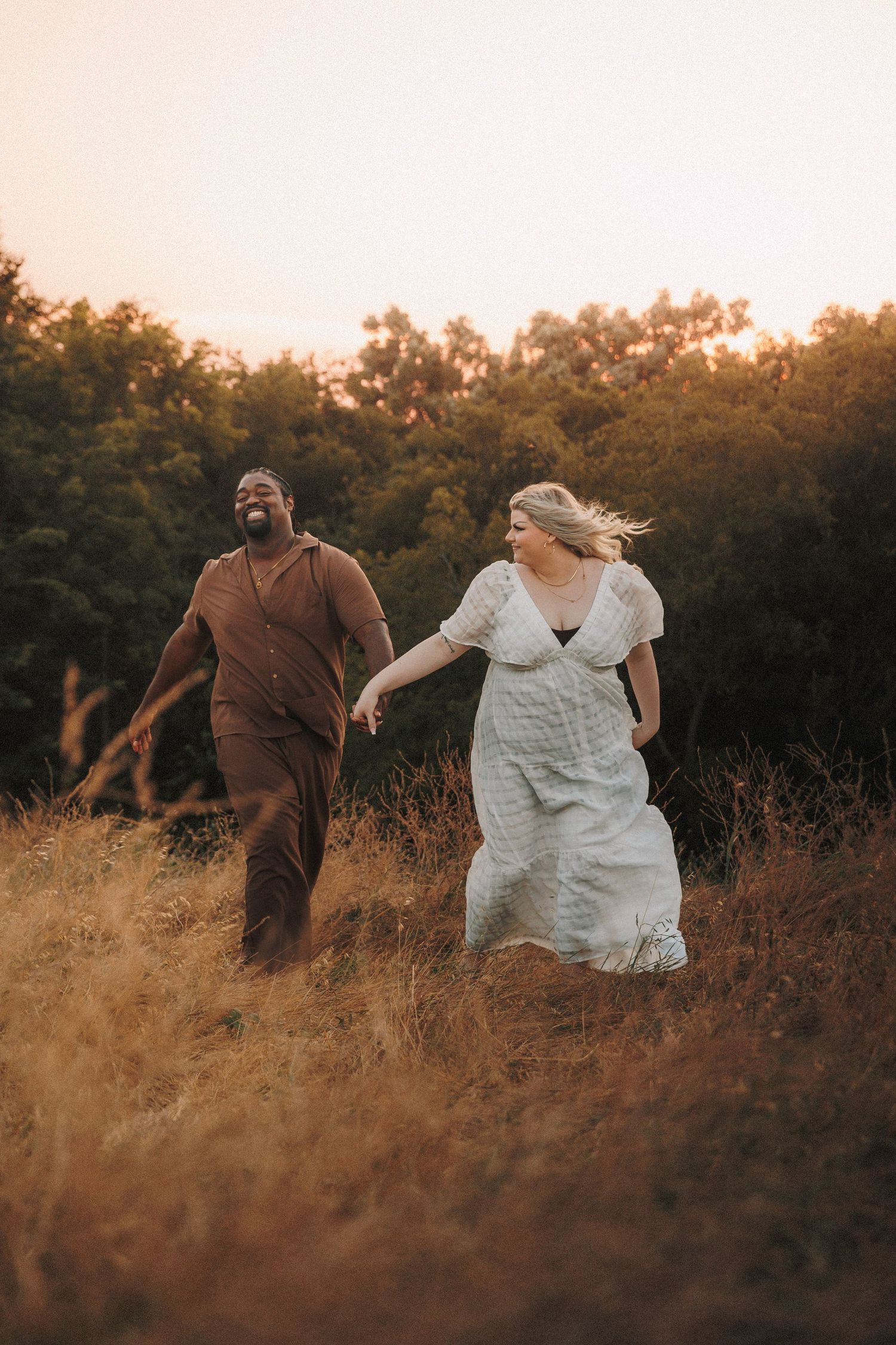 A couple dances playfully in a golden field at sunset creating a romantic silhouette against the warm evening light.