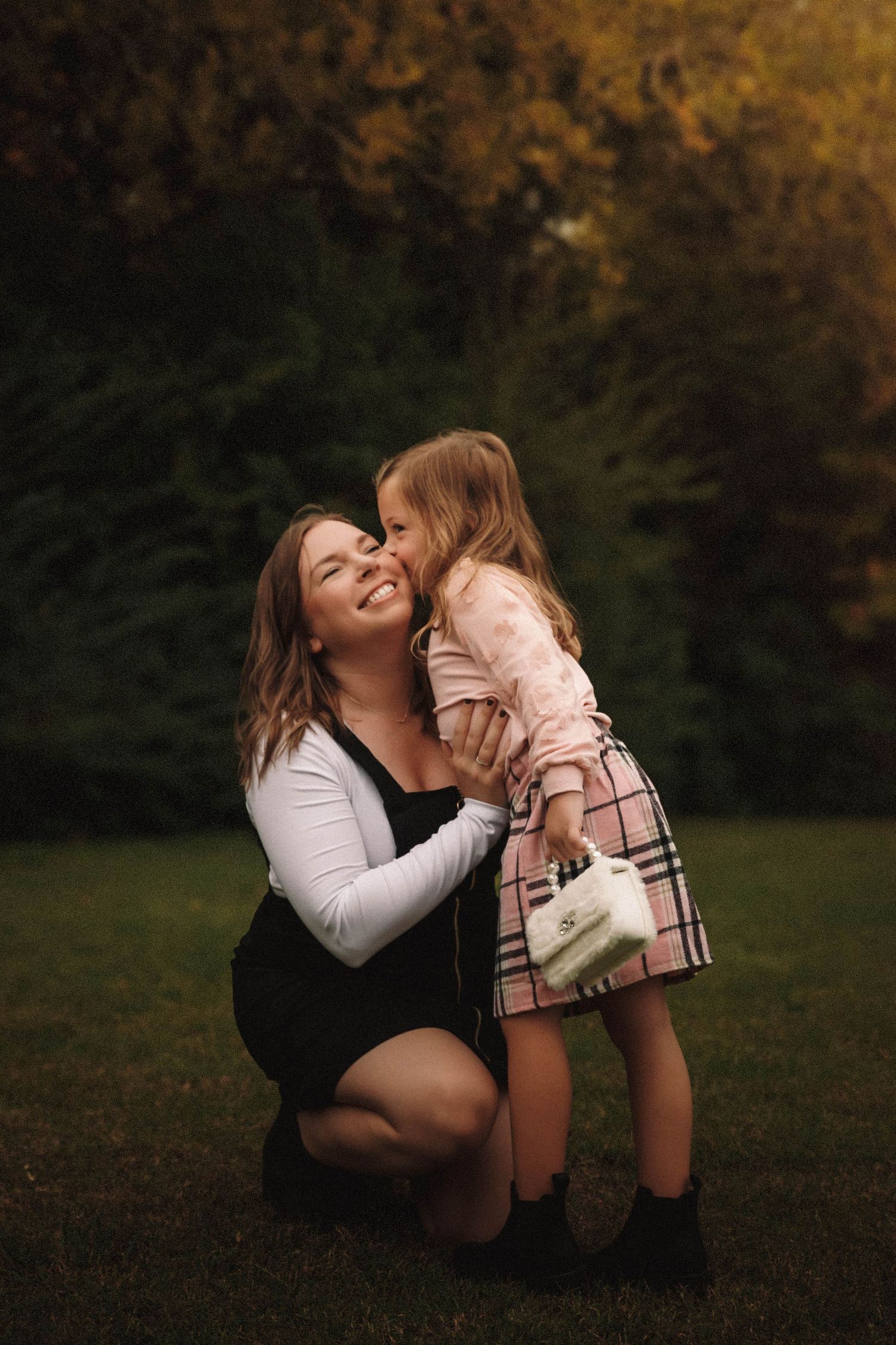Parent and child share a tender moment while sitting in grass during an autumn day.