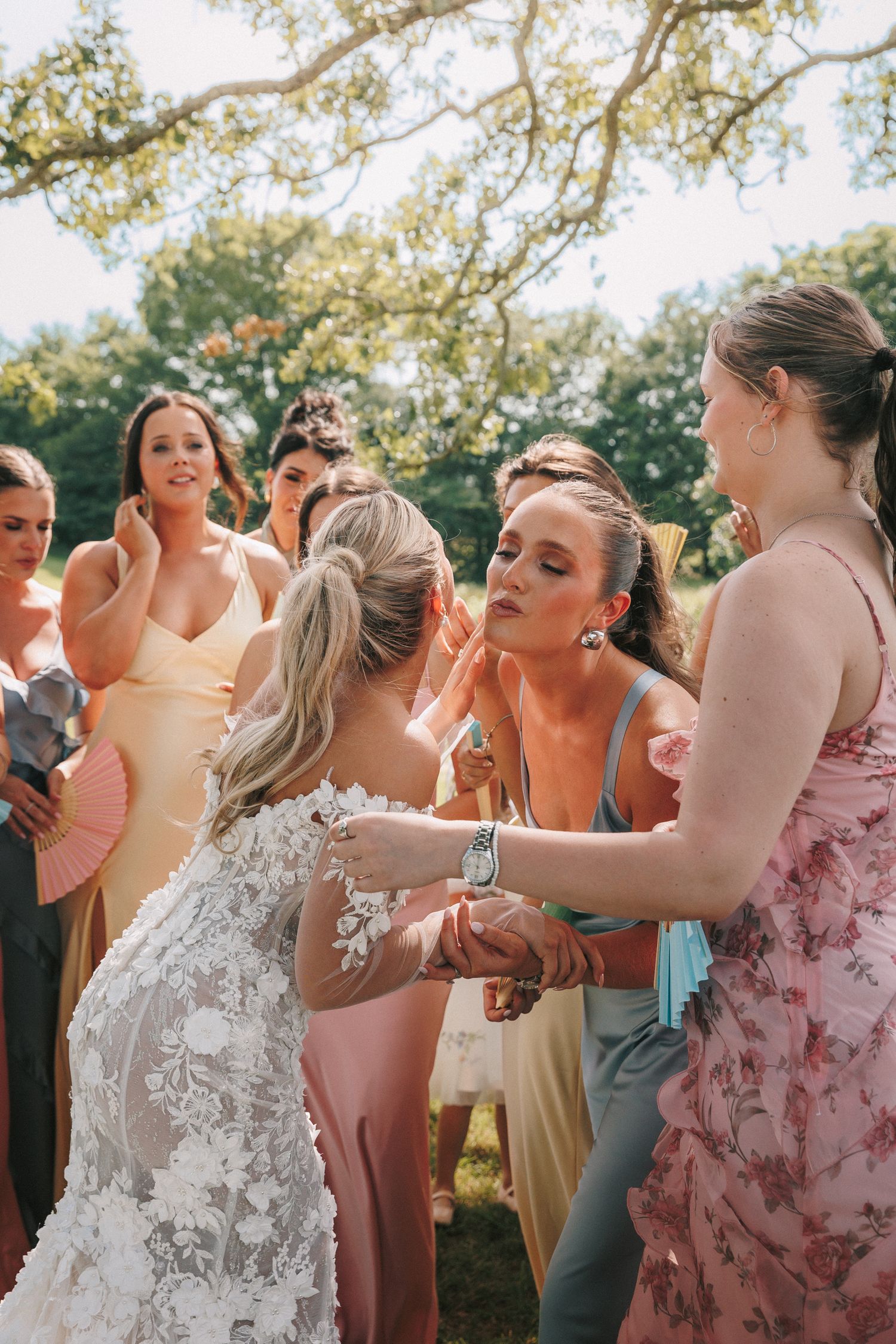 A group celebrates at an outdoor wedding reception in floral and pastel dresses.