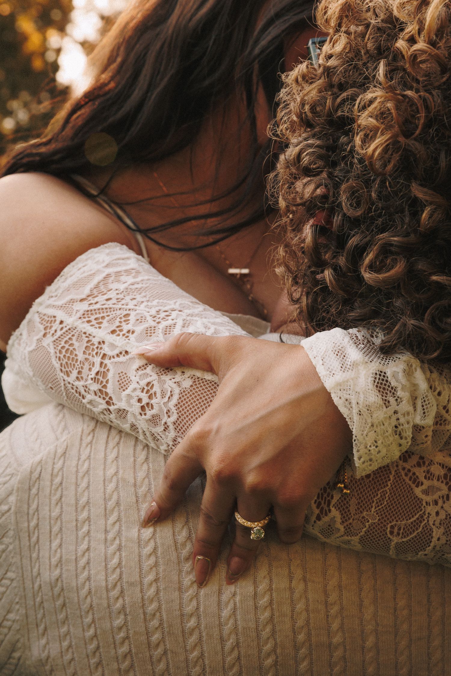 Close-up of hands resting on a cream-colored cable knit sweater with delicate lace details.