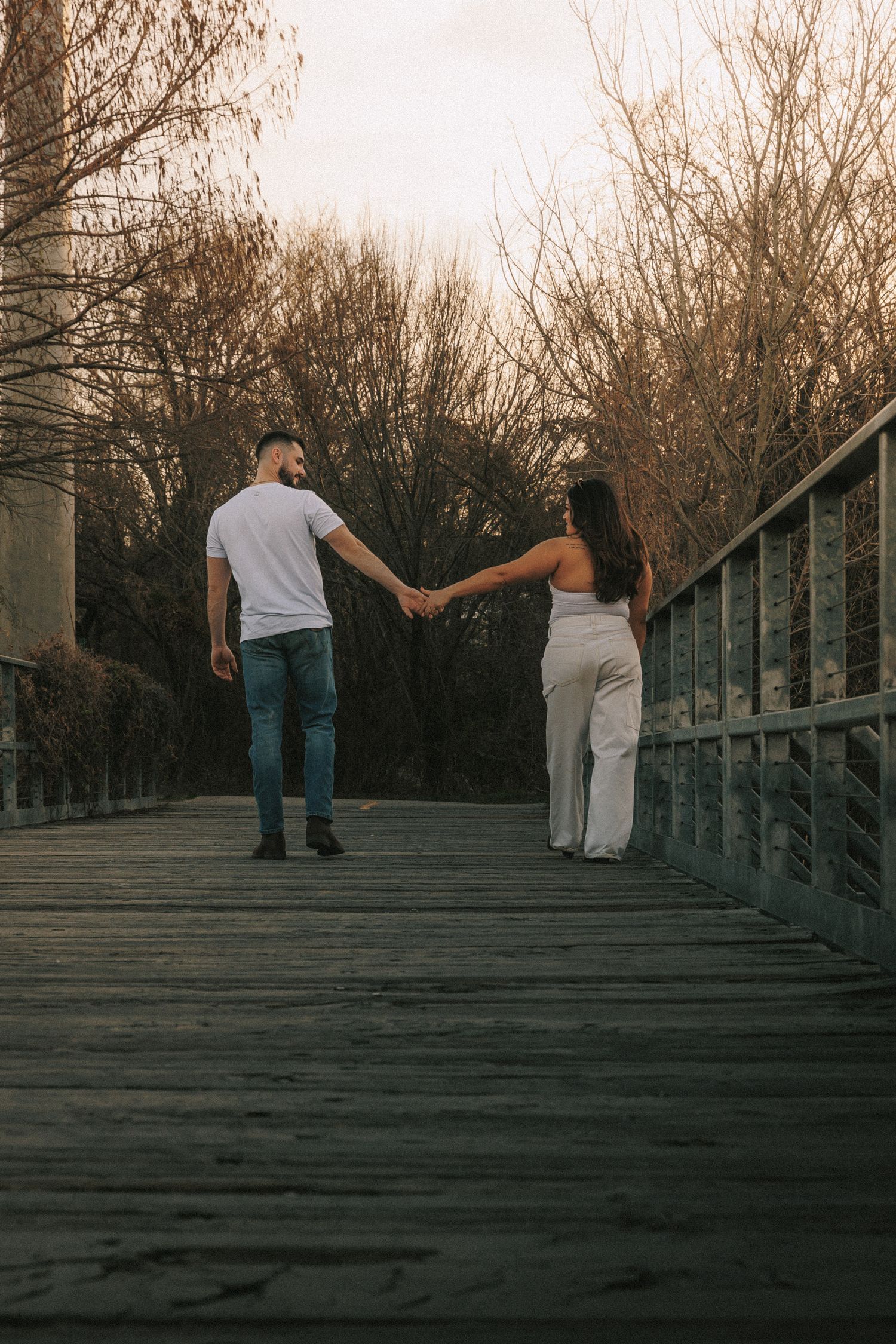 Couple walks up wooden stairs holding hands during sunset photo session.