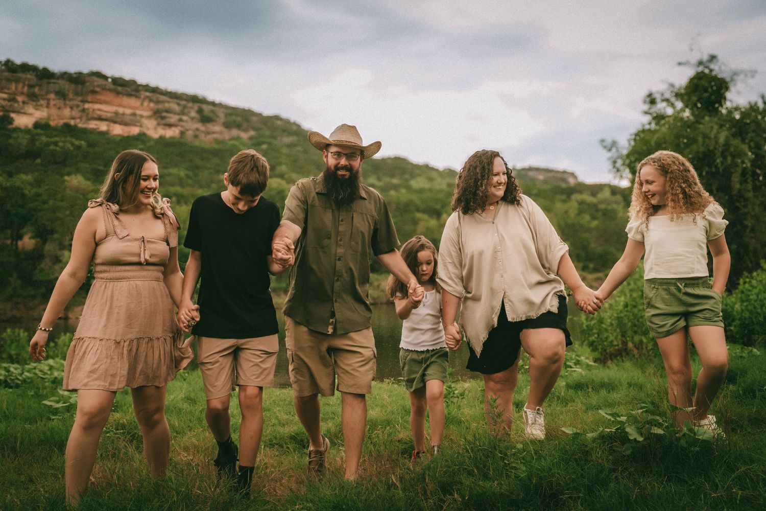 A group of people in coordinating beige outfits walking arm in arm through a green meadow at sunset.